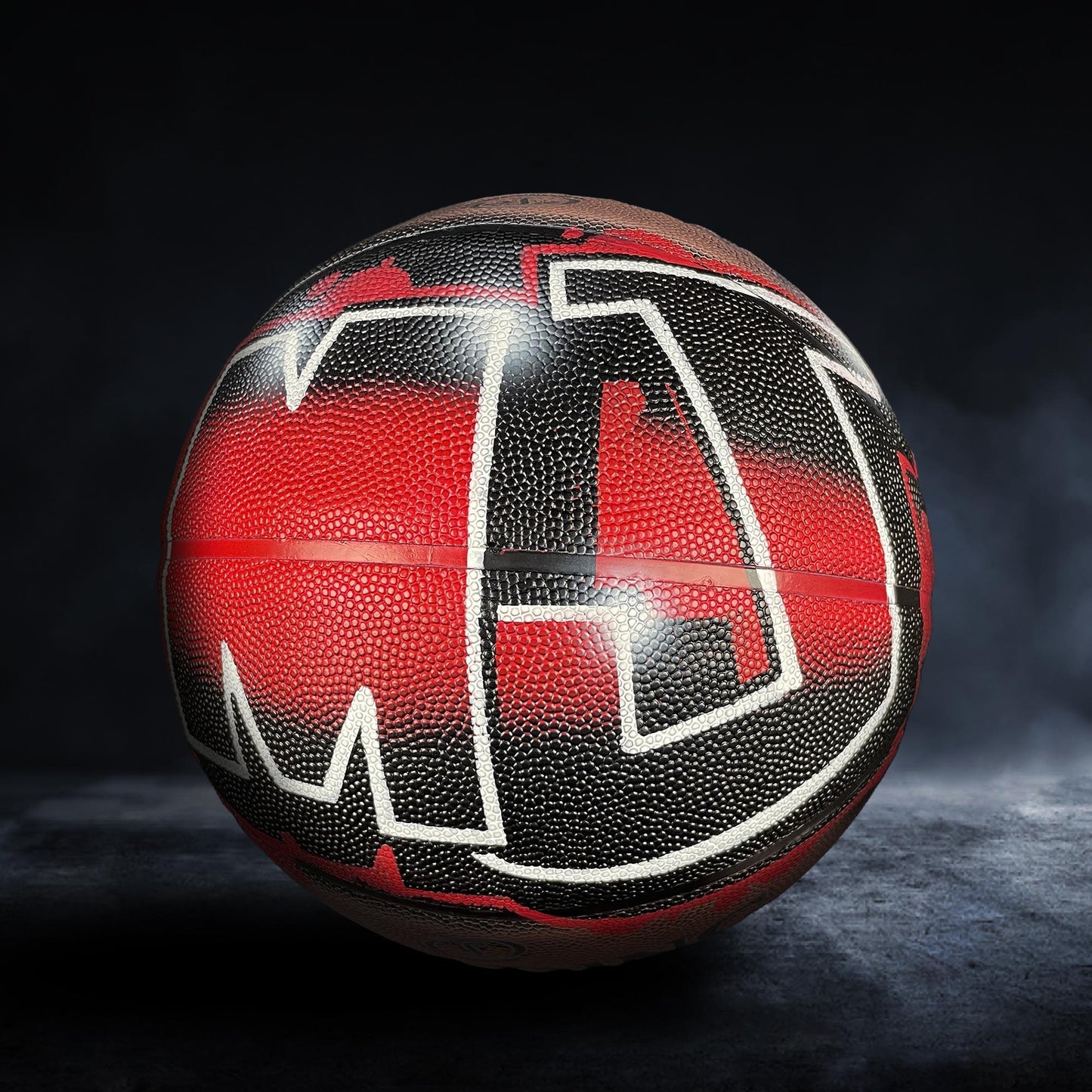 A basketball with a red and black textured surface, featuring the letters "M" and "J" prominently displayed.