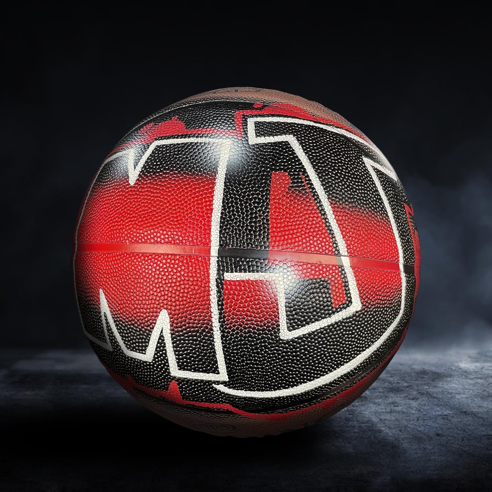 A basketball with a red and black textured surface, featuring the letters "M" and "J" prominently displayed.