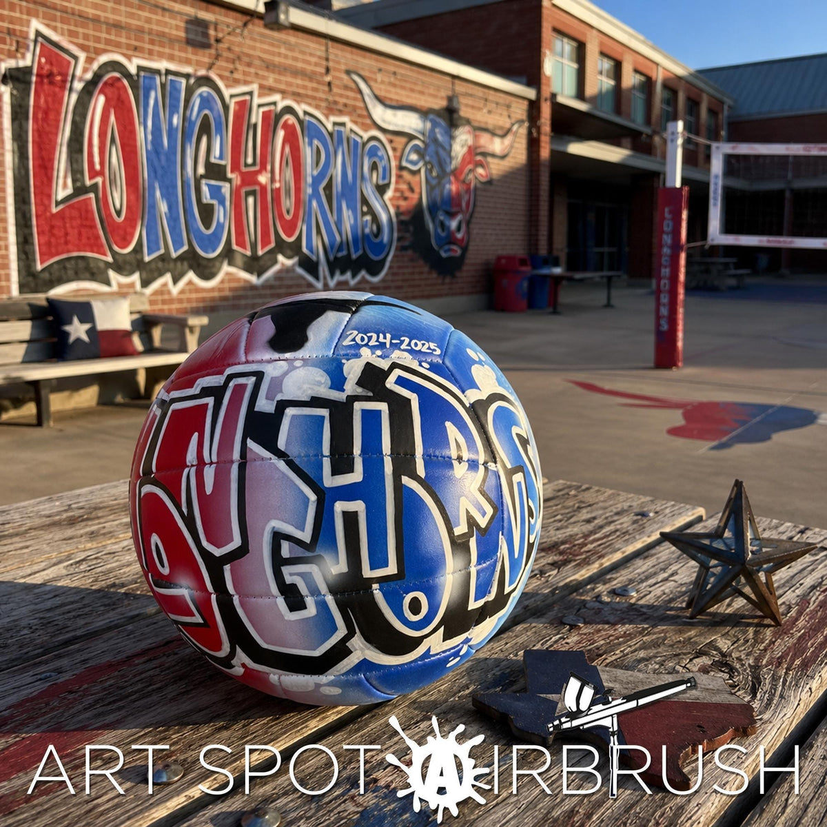 a custom volleyball personalized with graffiti on it, placed on a wooden surface, with a building and a mural in the background.
