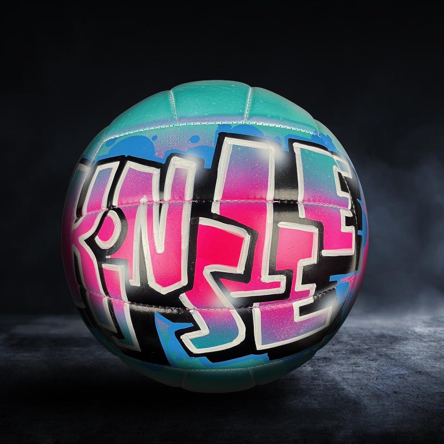 A colorful volleyball with graffiti-style text on it, set against a dark background.