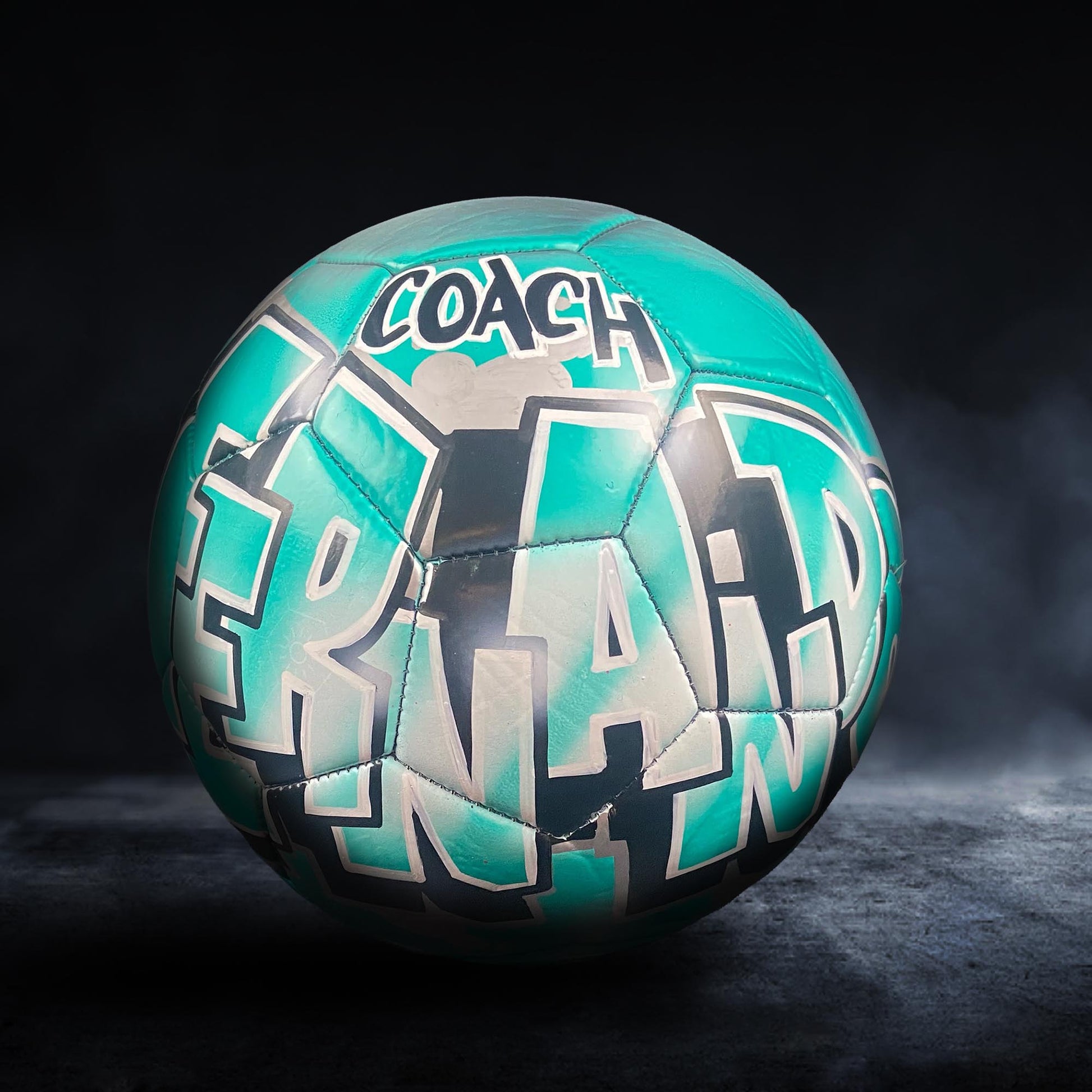 A soccer ball with the word "COACH" written on it in teal and white colors.