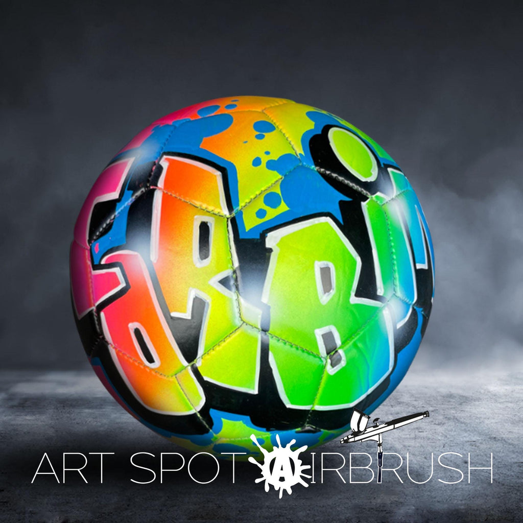 A colorful, graffiti-style soccer ball with the word "ART" painted on it, set against a dark background with smoke or fog.