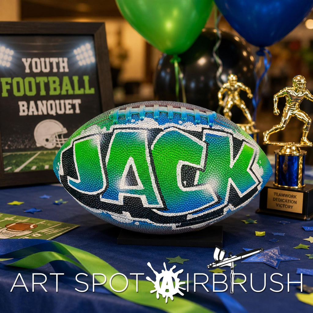 a custom football personalized with the name "JACK" painted on it, surrounded by various sports memorabilia such as a trophy, balloons, and a framed sign.