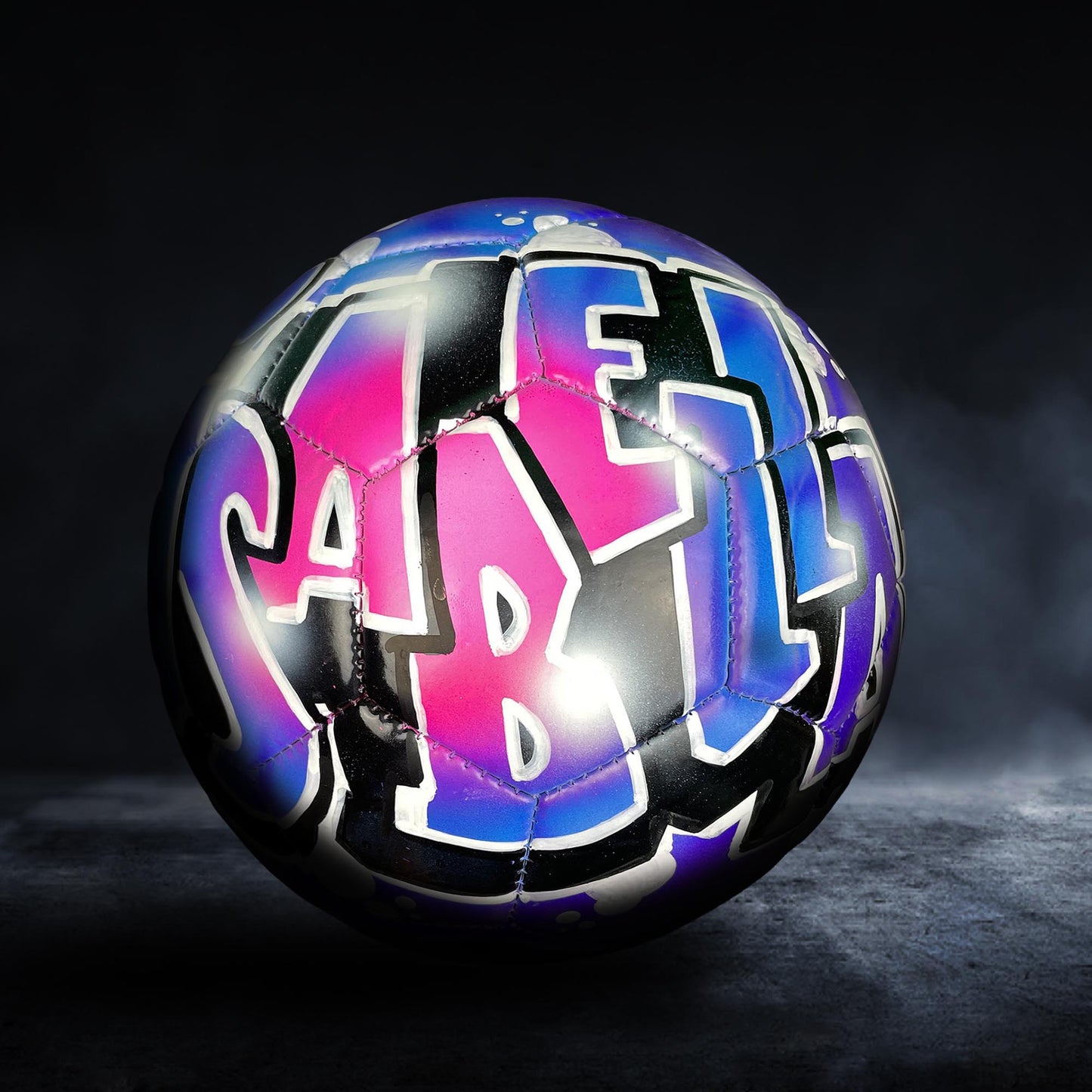 A colorful soccer ball with graffiti-style lettering on it, set against a dark background.