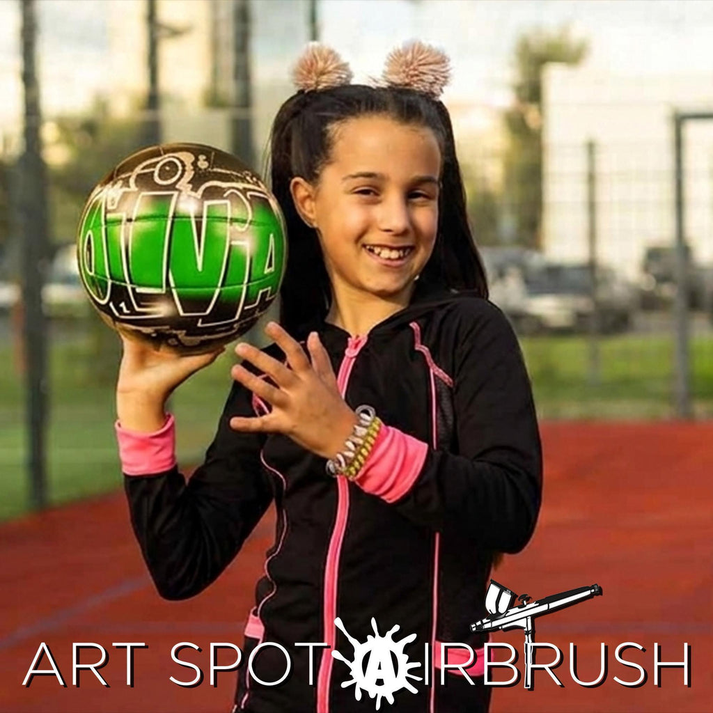 A young girl is holding a green custom volleyball with the word "OLIVIA" written on it, smiling and posing for the camera.