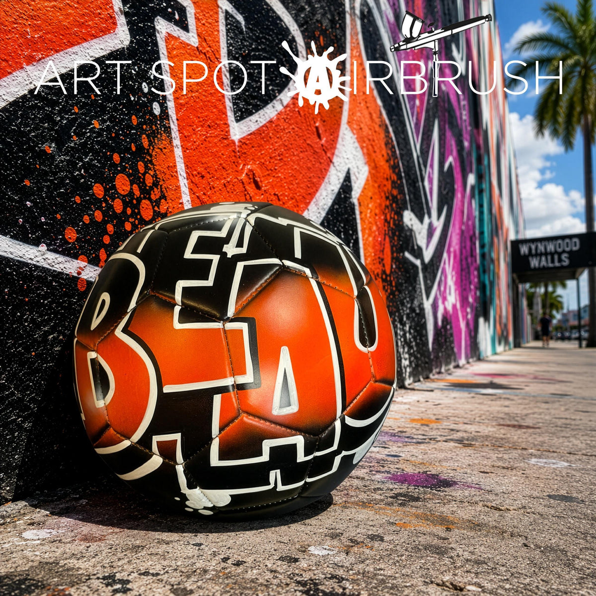 a soccer ball with the word "BEA" painted on it, placed against a colorful graffiti wall.