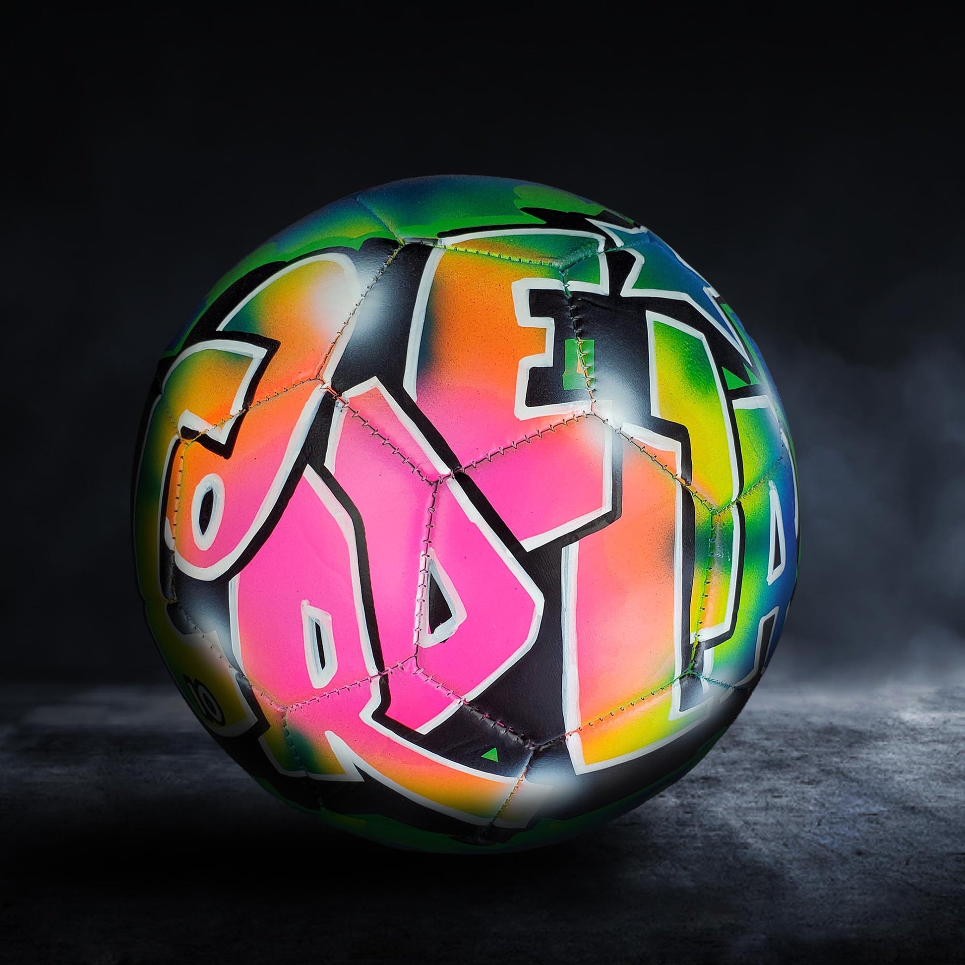 A colorful soccer ball with graffiti-style lettering on it, set against a dark background.