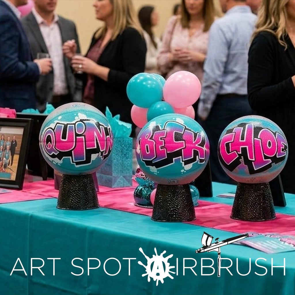 a table with three colorful sports balls, each with a unique name painted on them, surrounded by balloons and other decorations.