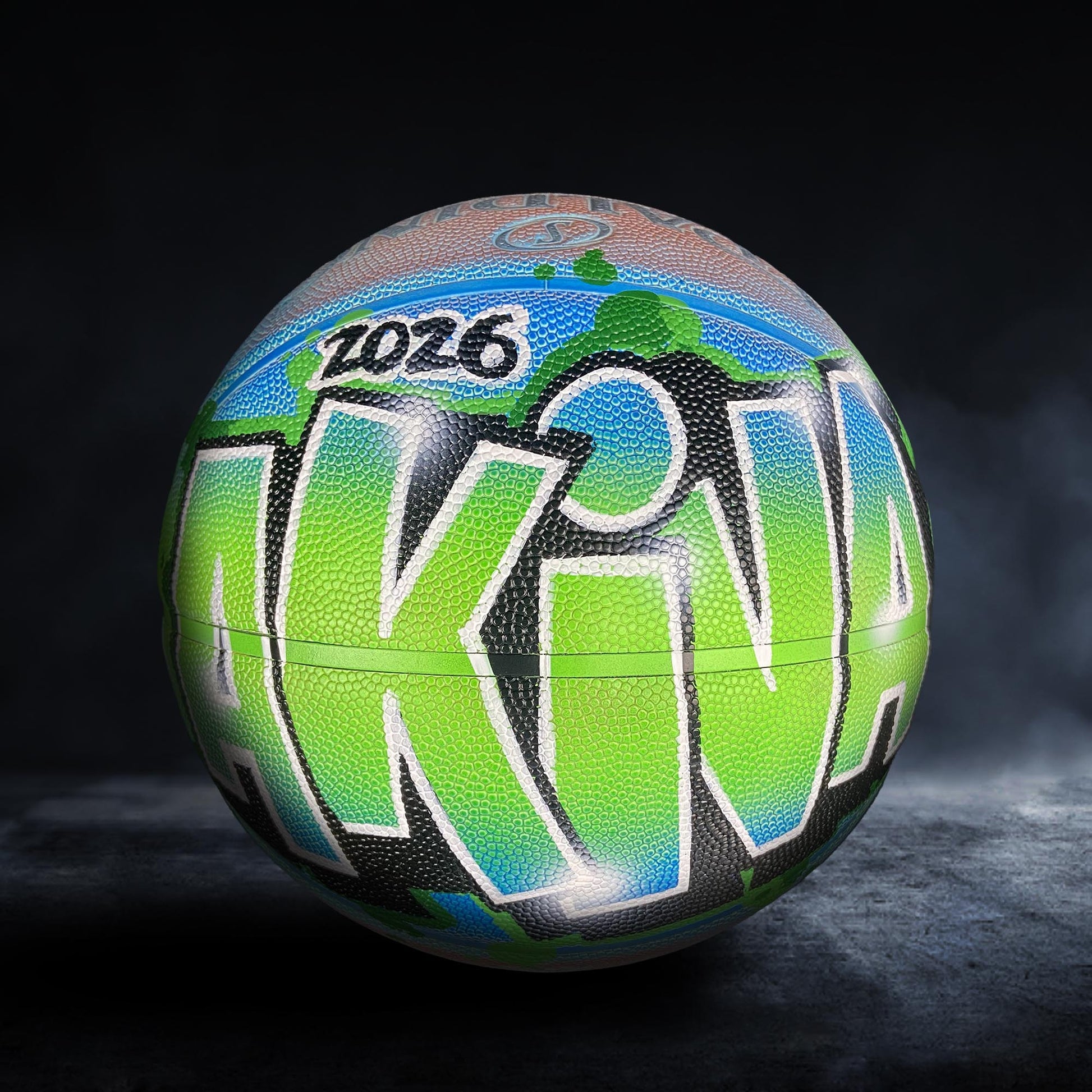 A colorful basketball with the word "AKINA" painted on it, featuring a mix of green, blue, and orange colors.