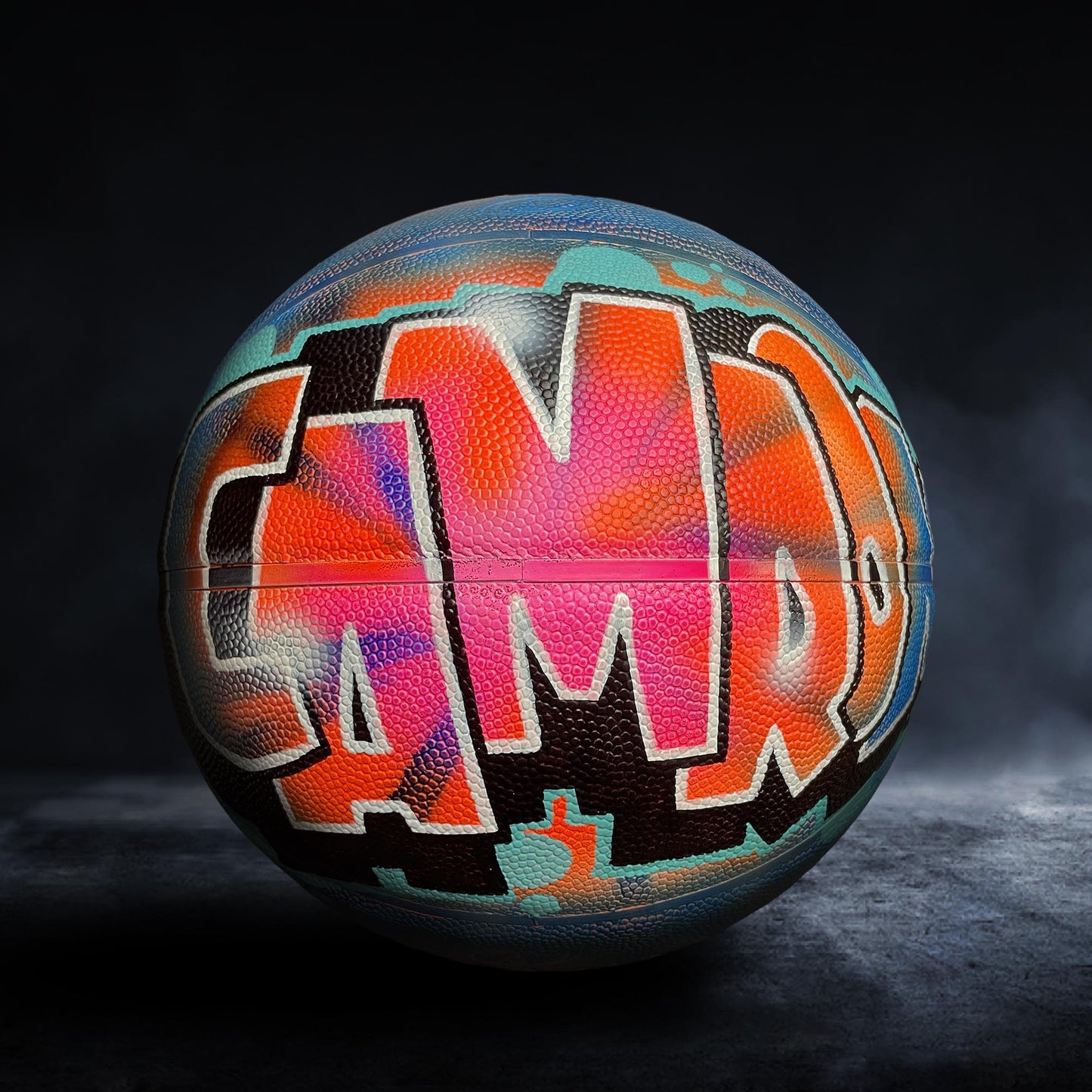 A basketball with the word "CAMP" painted on it in a colorful, graffiti-style design.