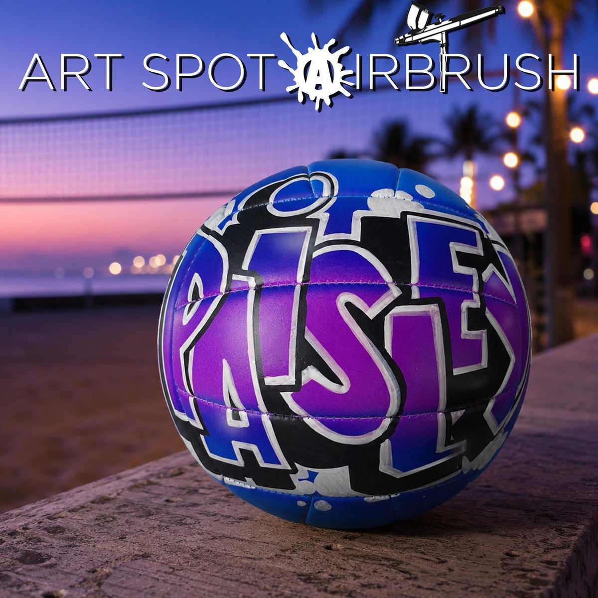 A purple and blue custom volleyball with the word "PAISLEY" written on it, placed on a wooden surface against a backdrop of a beach at sunset.