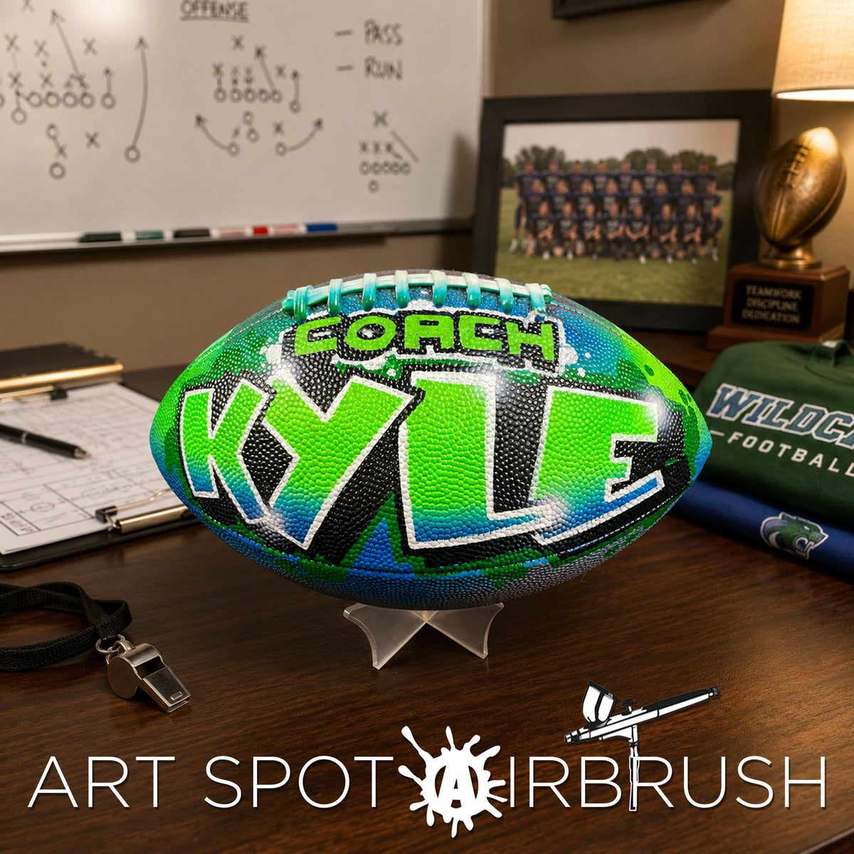 A custom football personalized with the name " Coach Kyle" on it, placed on a desk with various sports equipment and memorabilia.