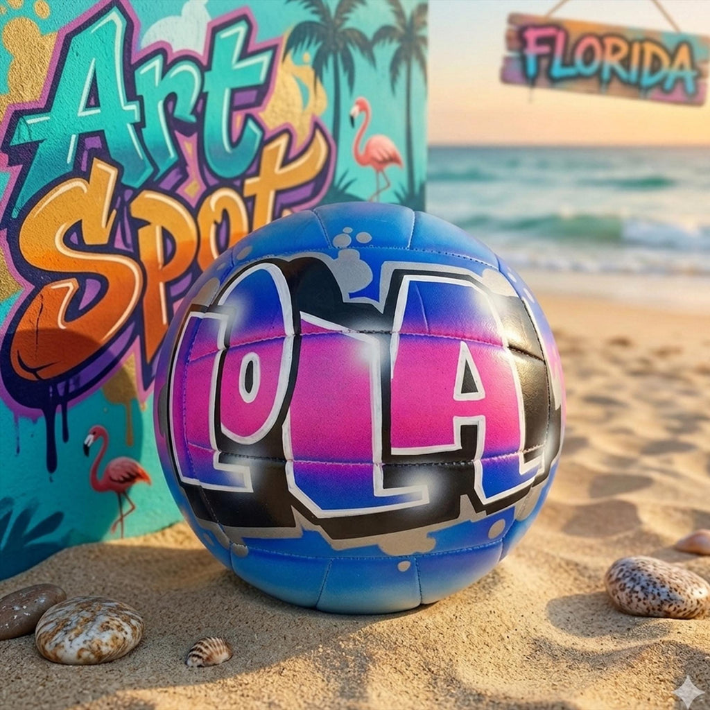 A colorful graffiti-style sign reading "Art Spot" is displayed on a beach, with a volleyball featuring the word "LA" in the foreground.