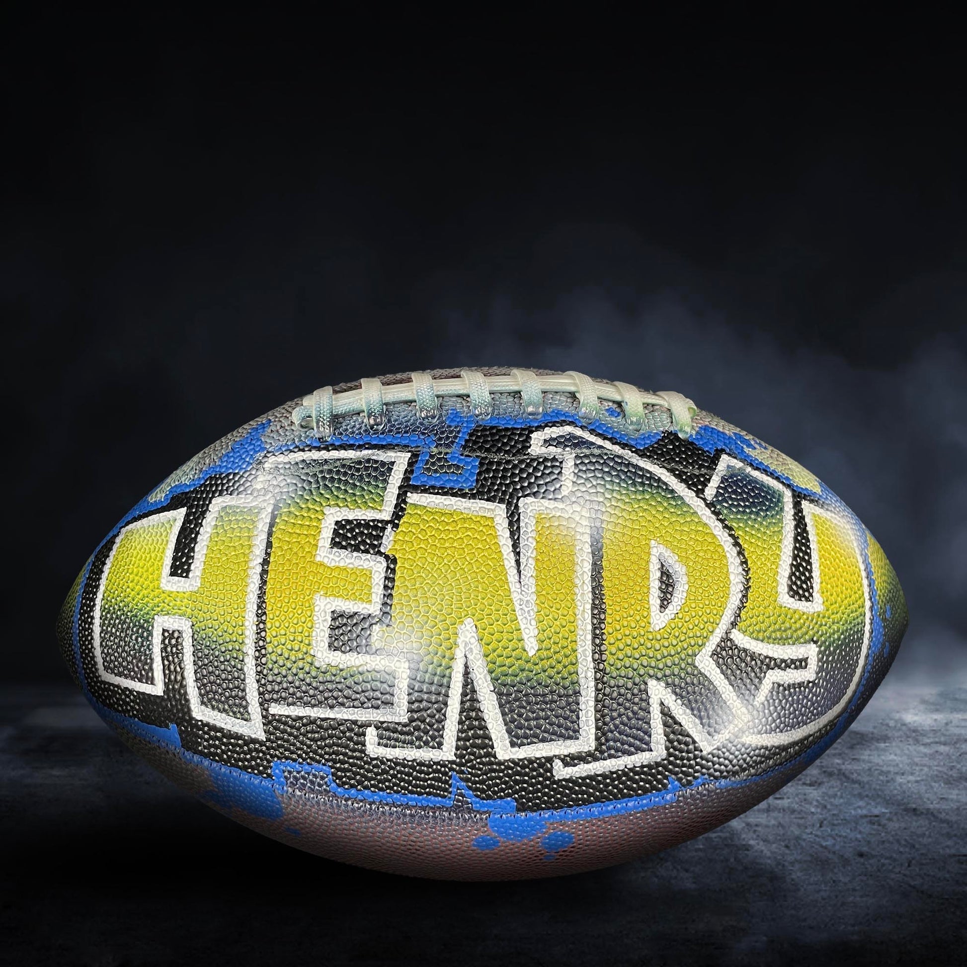 A football with the name "HENRY" painted on it, set against a dark background with smoke or fog.
