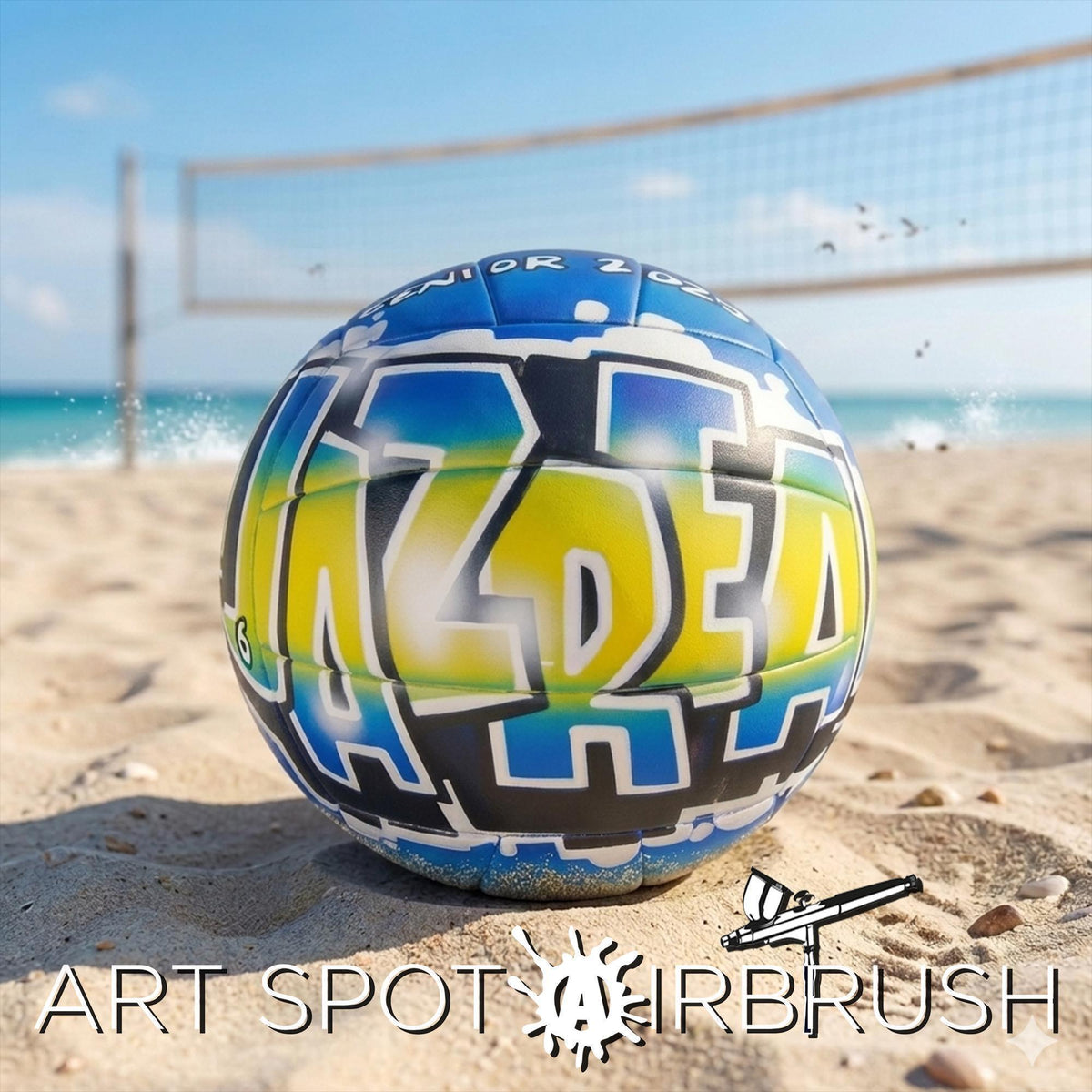 A colorful beach custom volleyball with the word "Jazrea" painted on it, sitting on the sand near a volleyball net.