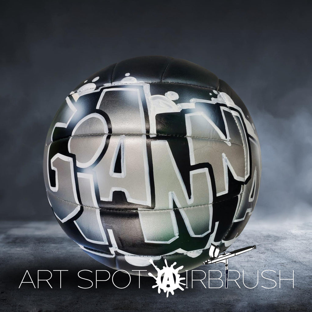 A black and white soccer ball with graffiti-style text on it, placed on a dark surface.