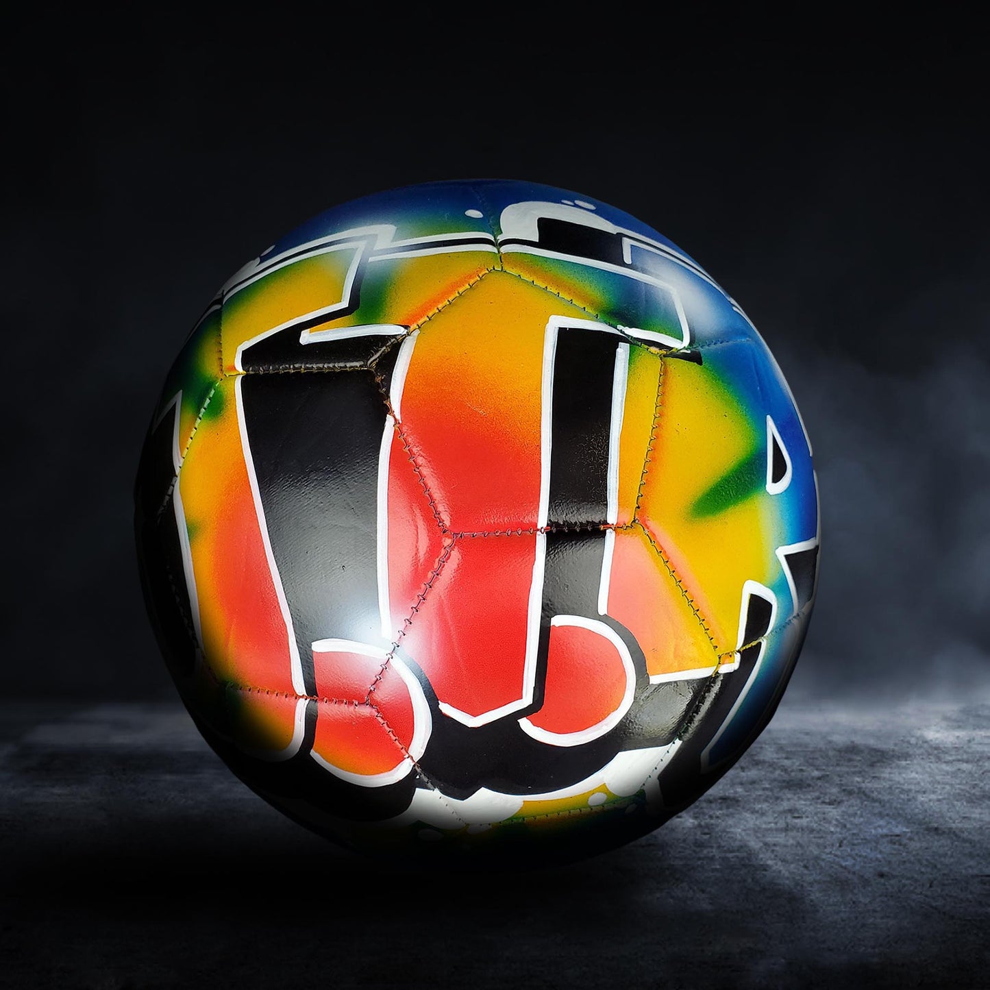 A colorful soccer ball with a vibrant, graffiti-style design on it, set against a dark background.