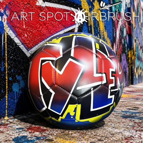 A soccer ball with graffiti-style lettering is displayed against a colorful, graffiti-covered wall.