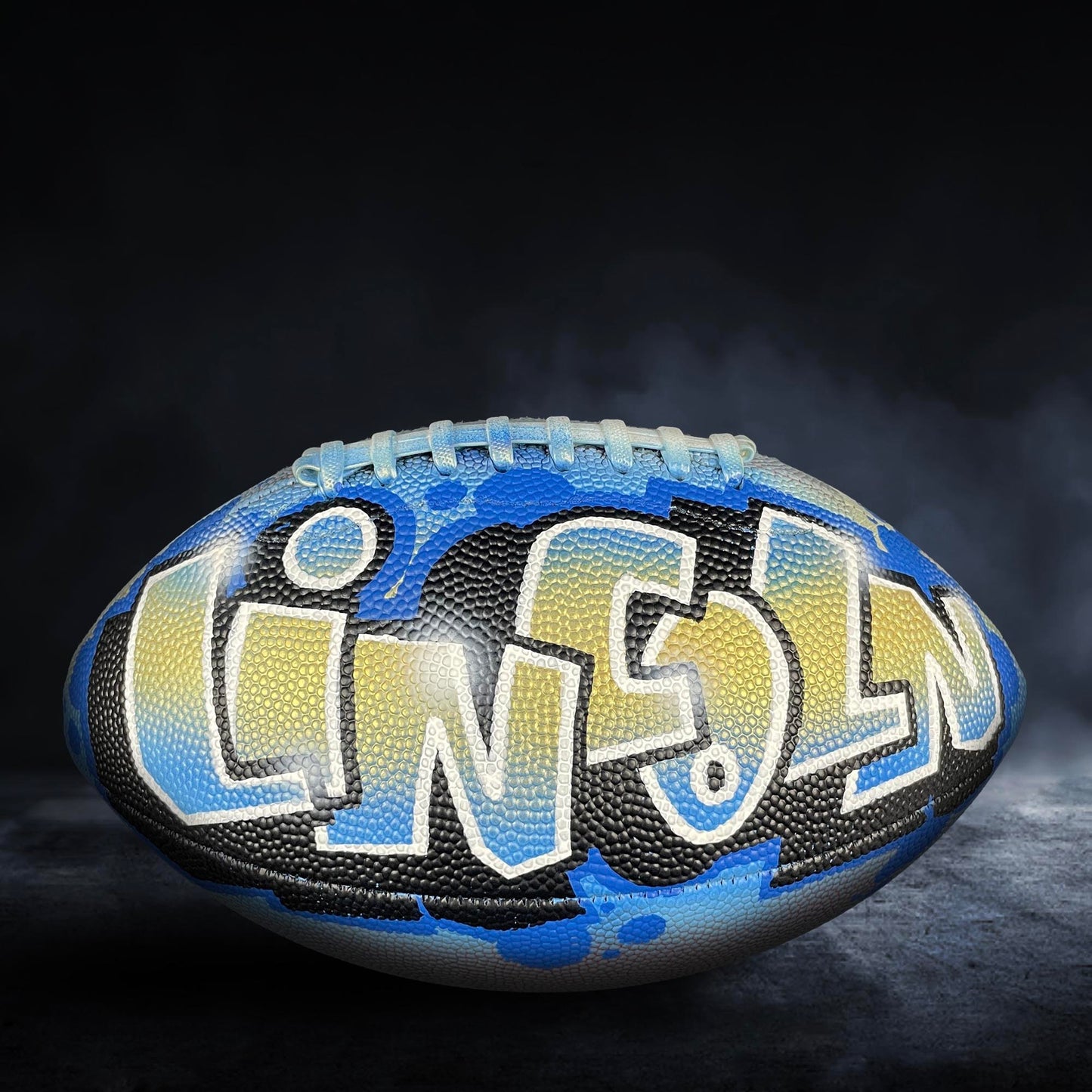 A football with the word "LINCOLN" painted on it, against a dark background with smoke or fog.