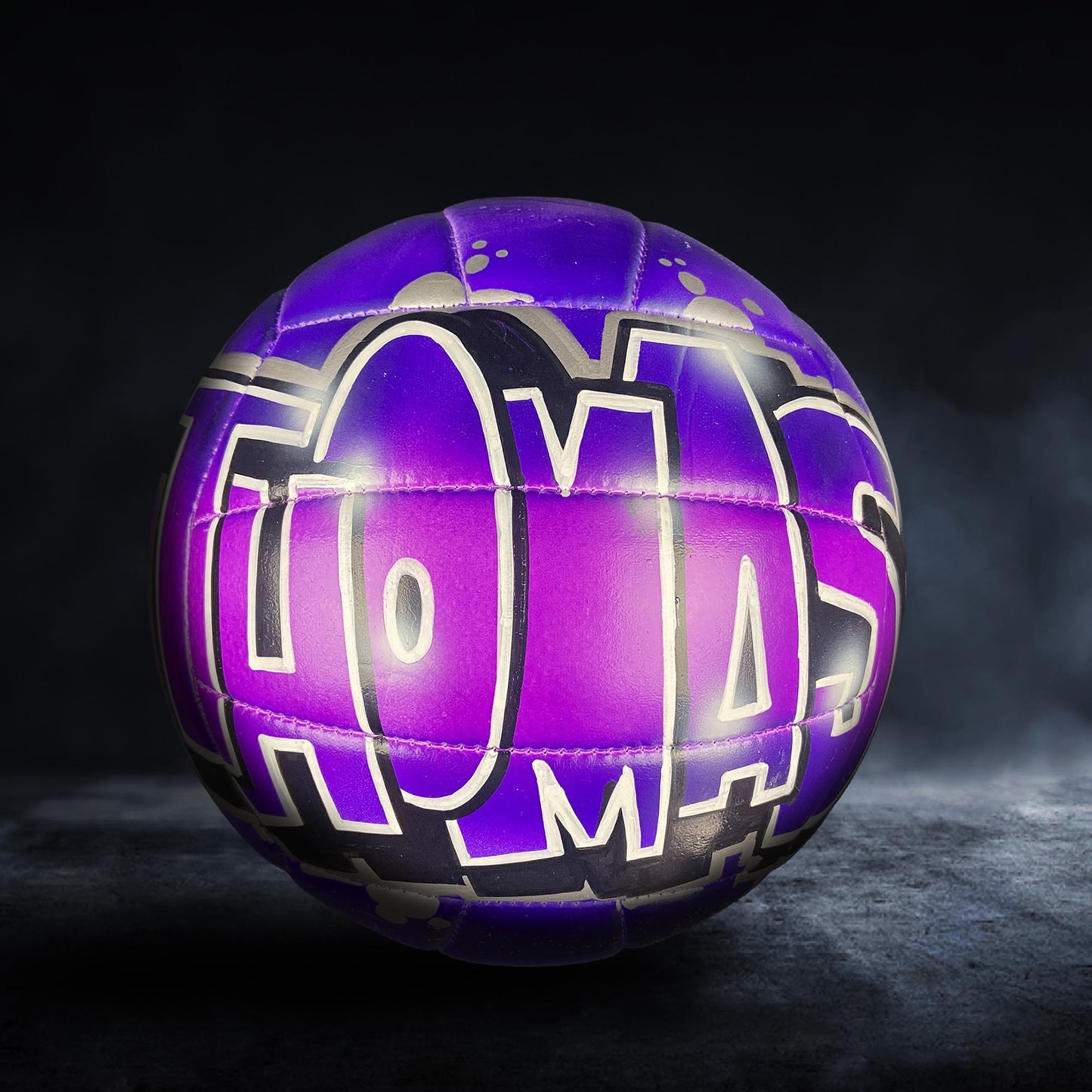 A purple and black soccer ball with the word "Thomas" written on it.