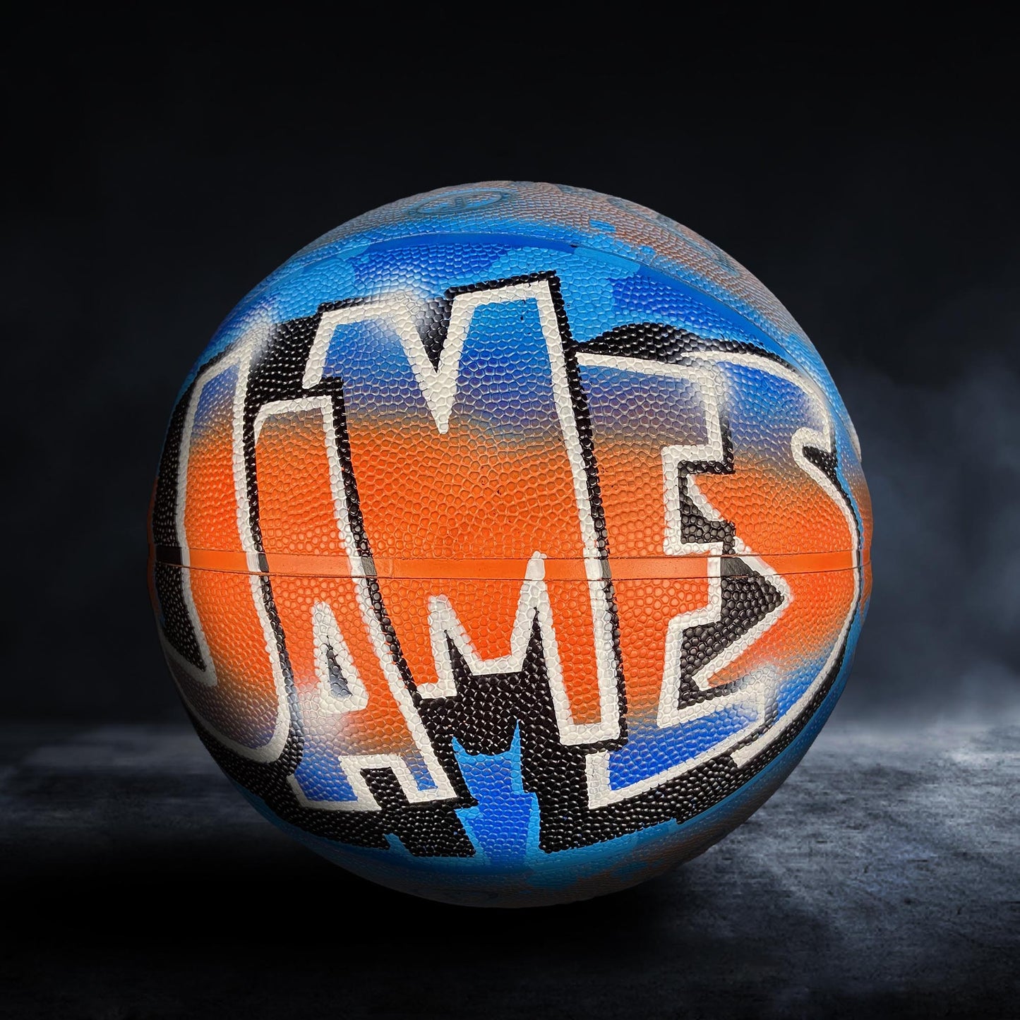 A basketball with the word "JAMES" painted on it in a colorful, graffiti-style design.