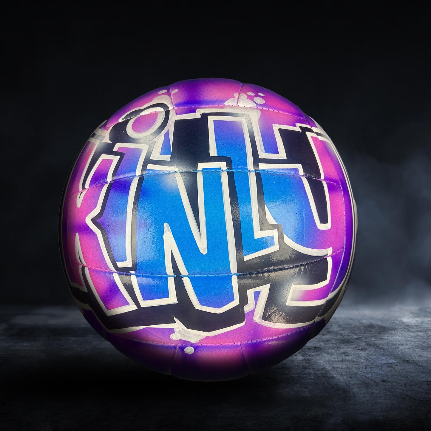 A colorful sports ball with graffiti-style text on it, set against a dark background.