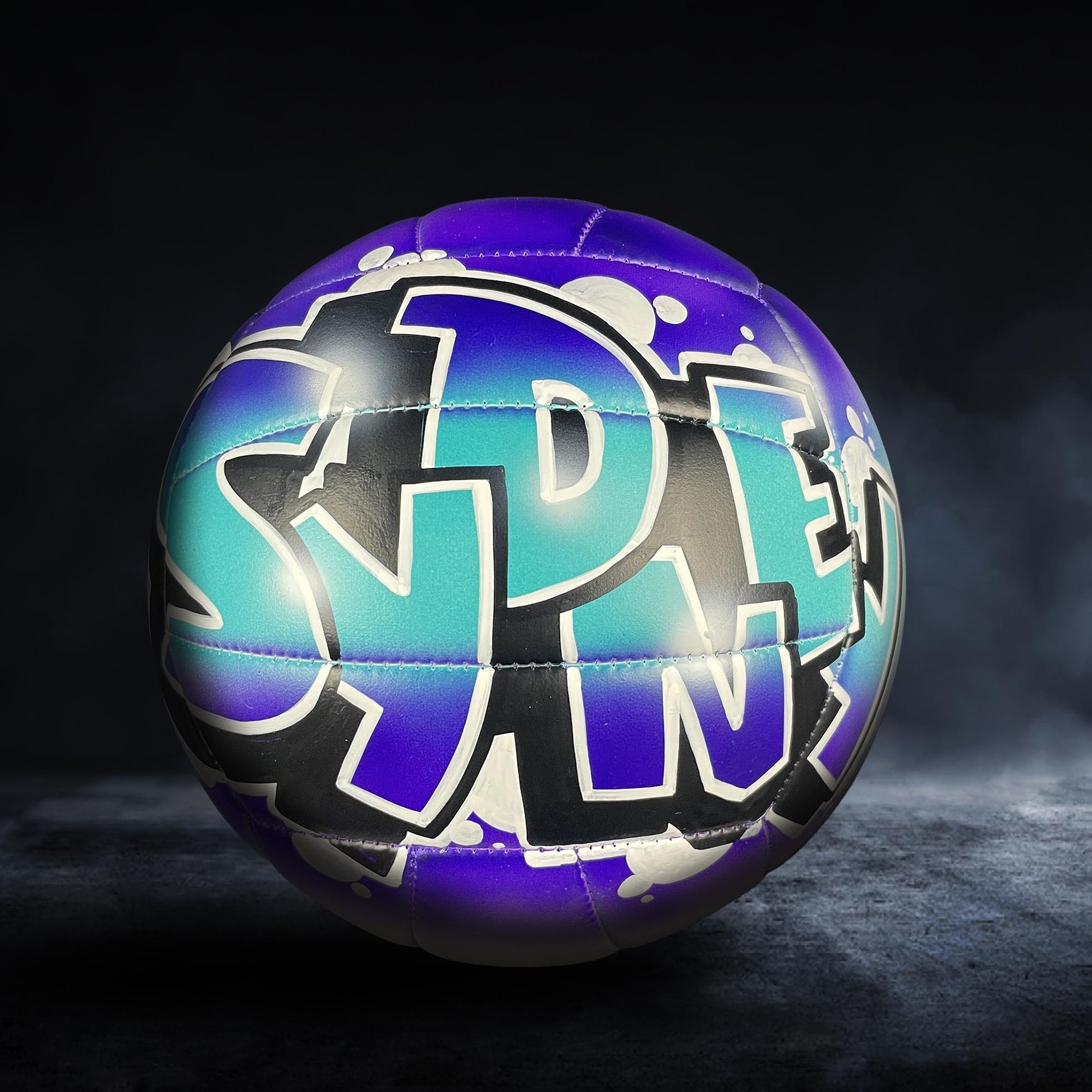 A colorful sports ball with graffiti-style text on it, set against a dark background.