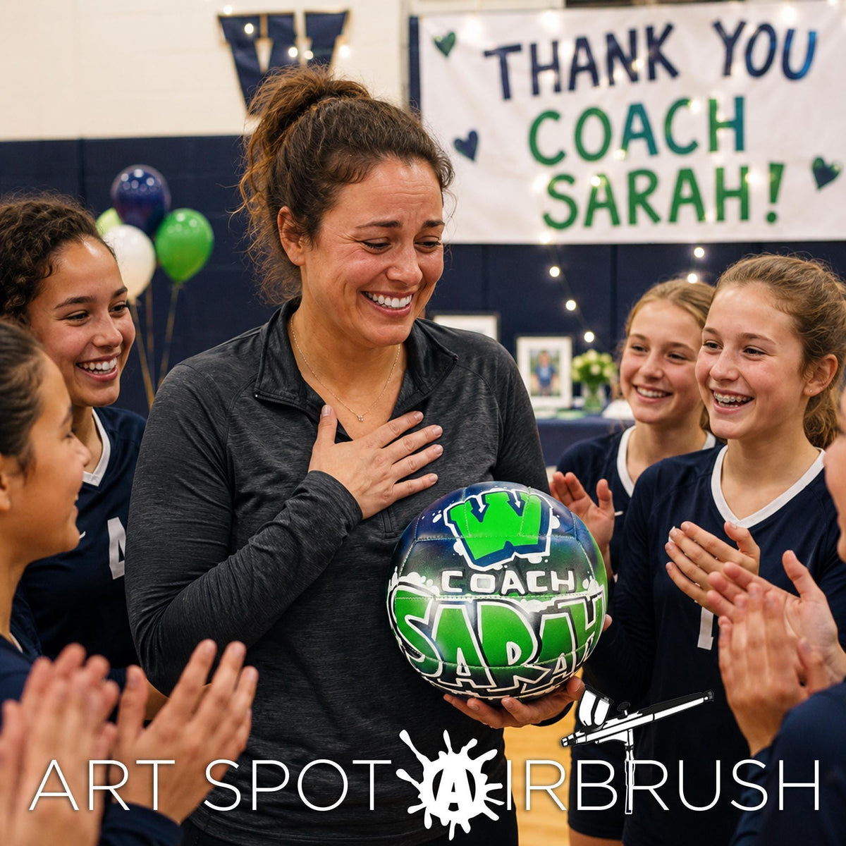 A group of young women are gathered around a woman holding a sports ball with the word "COACH" on it, who is smiling and clapping.