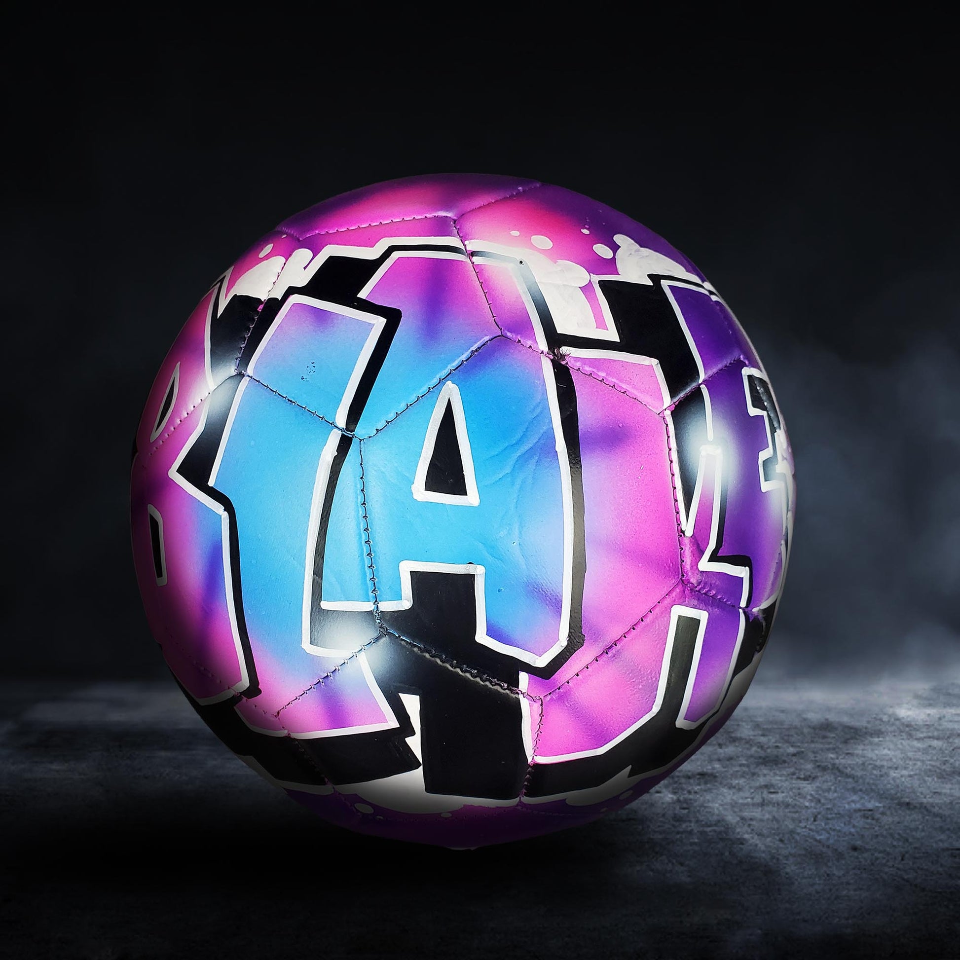 A colorful soccer ball with graffiti-style lettering on it, set against a dark background.