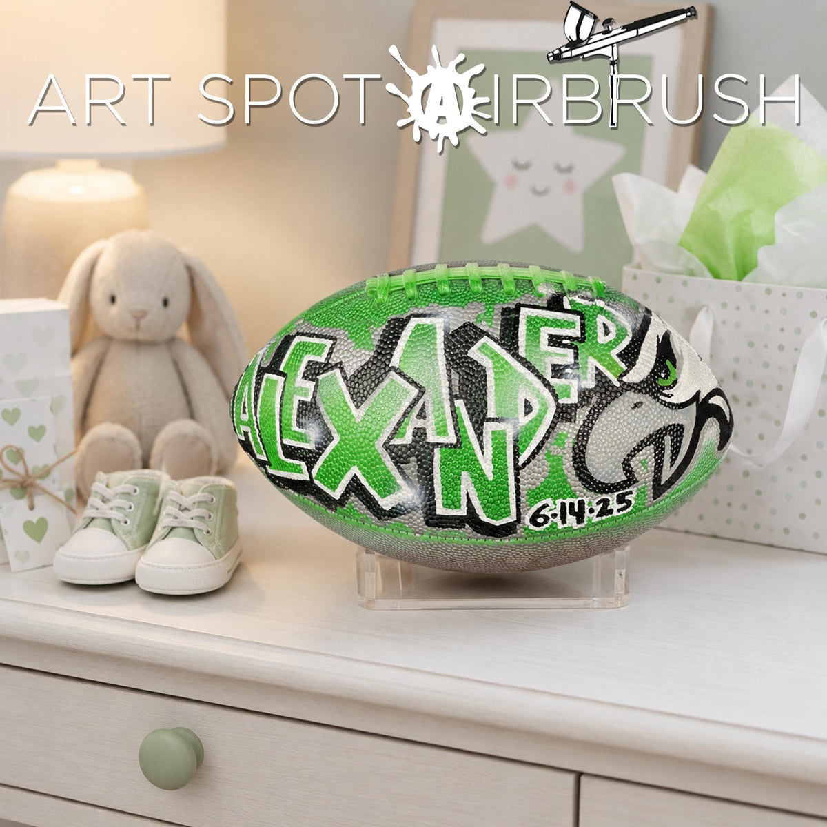 a personalized football with the name "ALEXANDER" painted on it, placed on a white dresser next to a pair of baby shoes.