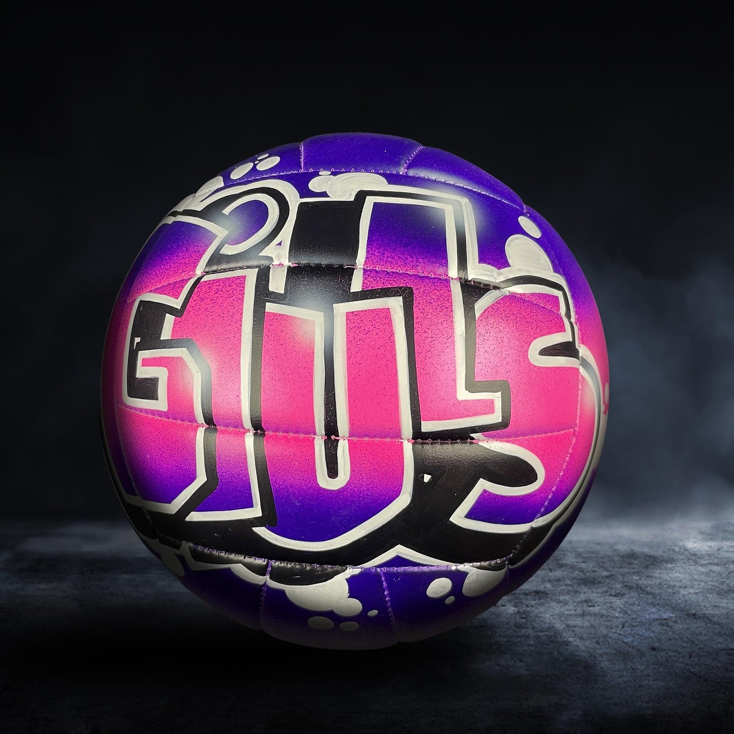 A colorful volleyball with the word "GUS" painted on it, set against a dark background.