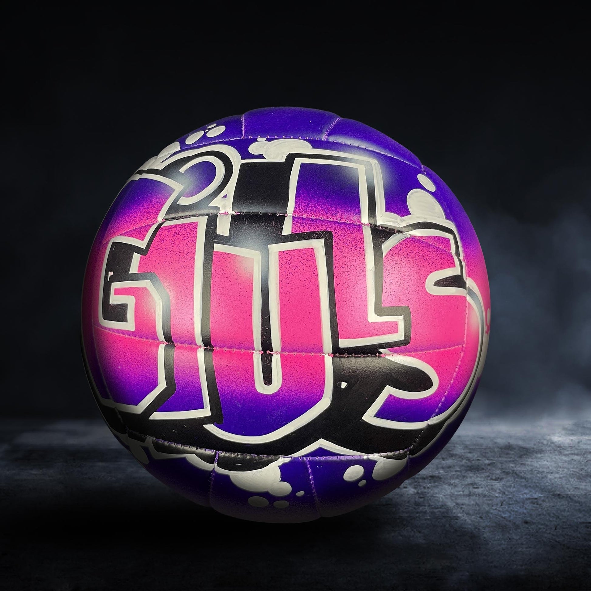 A colorful volleyball with the word "GUS" painted on it, set against a dark background.