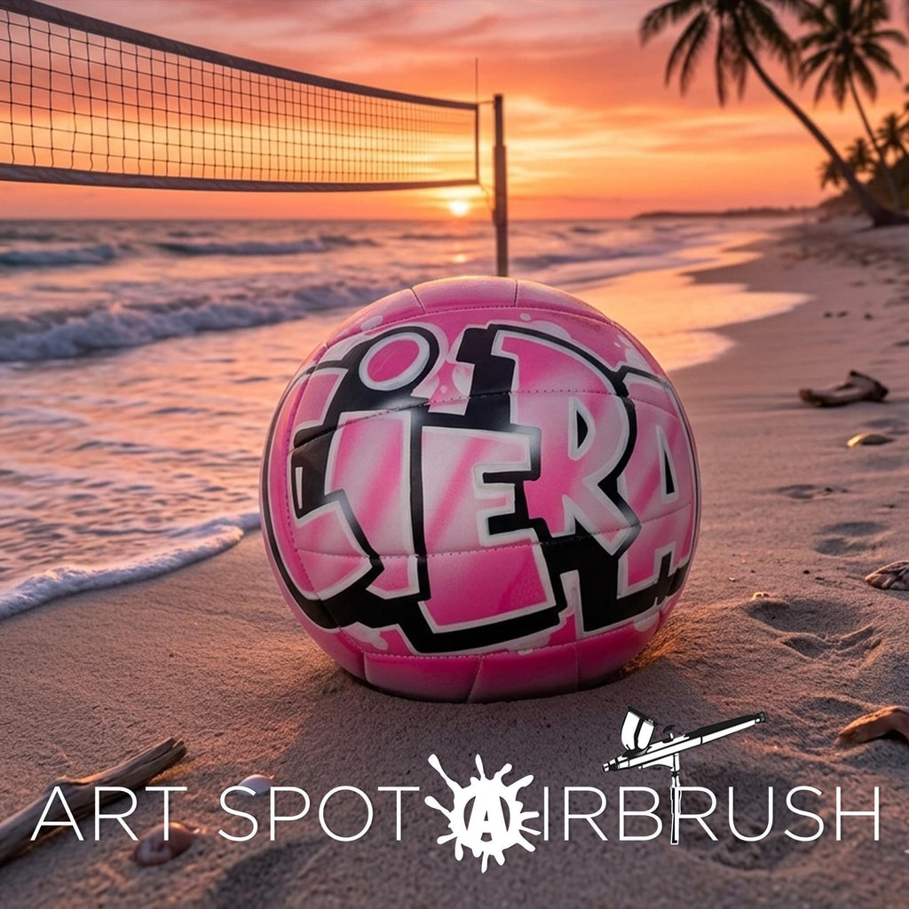 A pink custom volleyball personalized with the word "Ciera" written on it, placed on a sandy beach with palm trees and a sunset in the background.