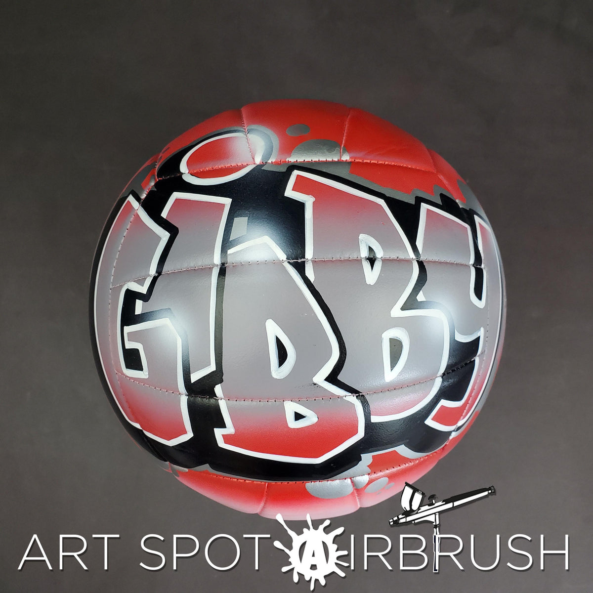 A red and black volleyball with the word "GIBBY" painted on it, along with a logo for "ART SPOT AIRBRUSH".