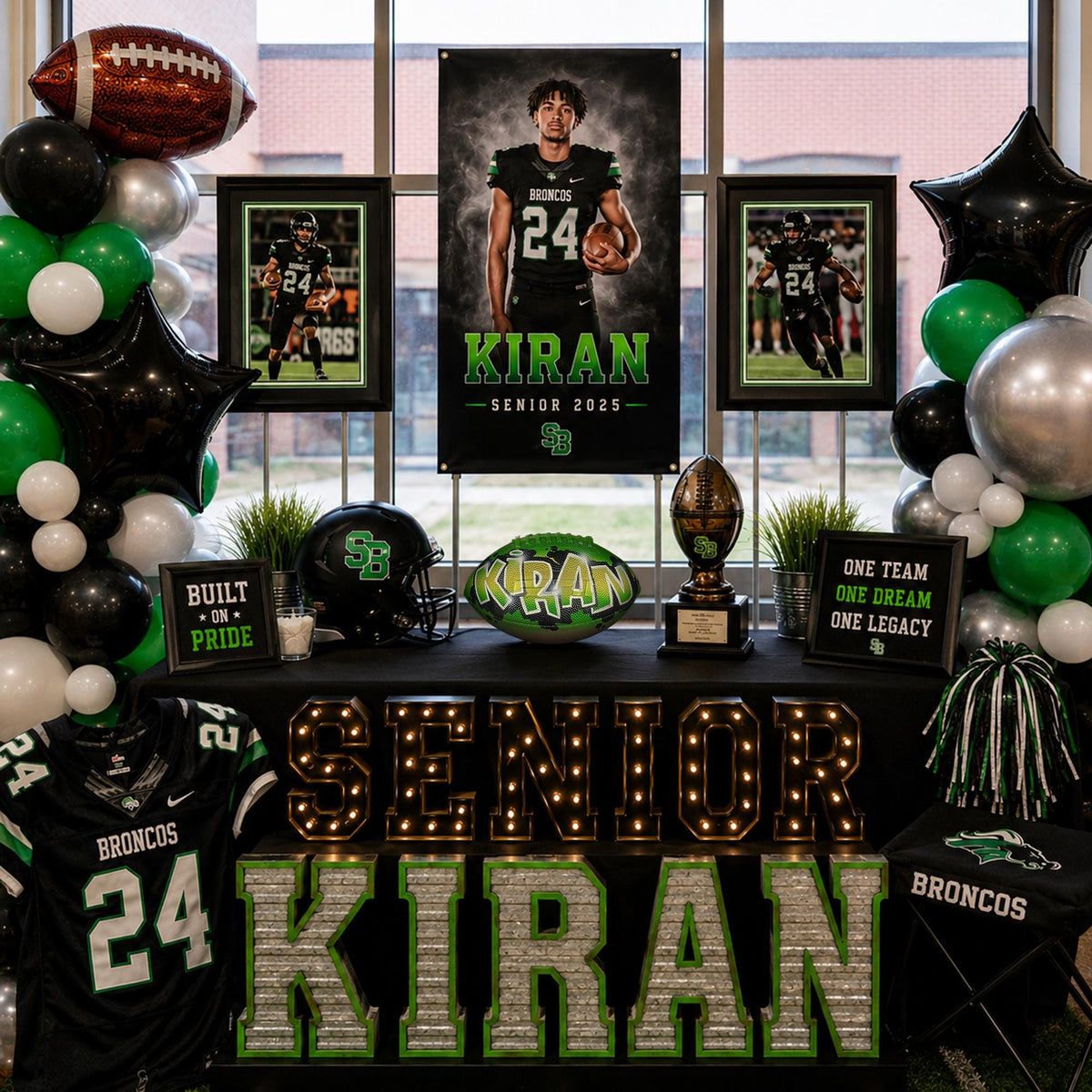 The image is a display celebrating the graduation of a football player named KIRAN. The display includes a framed photo of KIRAN, a football helmet, a trophy, and a banner that reads "SENIOR KIRAN". The display is decorated with green and white balloons, and the football player's jersey is visible.