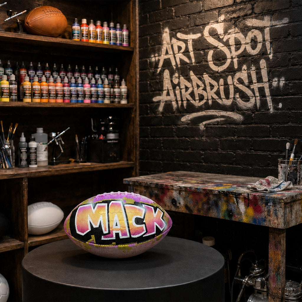 a custom football personalized with the name "MACK" painted on it, placed on a table in front of a graffiti-covered wall.