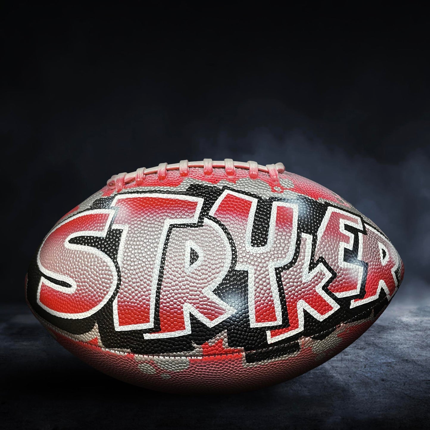A football with the word "STRYKER" painted on it, against a dark background with smoke.