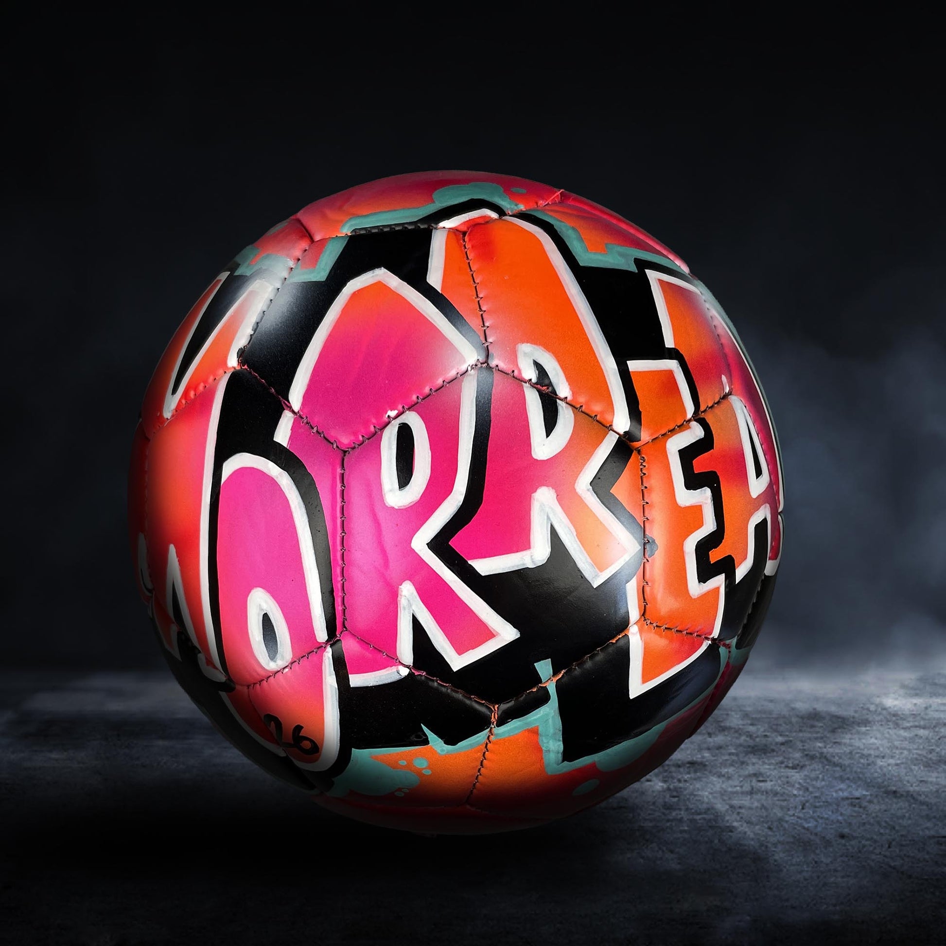 A colorful soccer ball with graffiti-style text on it, set against a dark background.