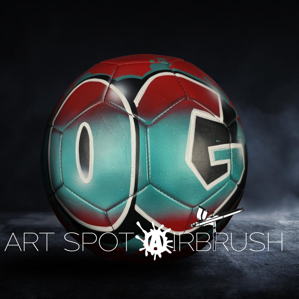 A soccer ball with the letters "OG" painted on it, set against a dark background with a misty or foggy effect.