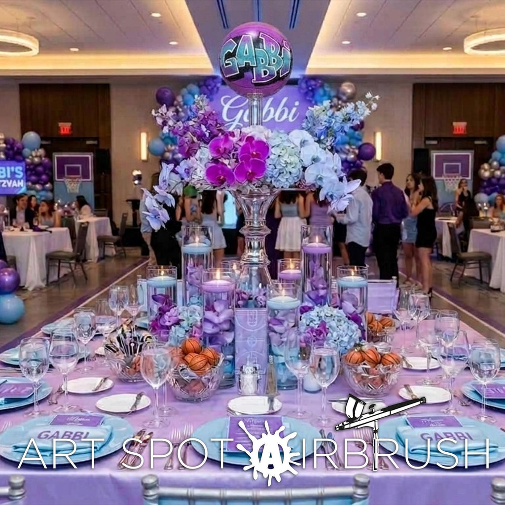 The image is a beautifully decorated event space with a large floral centerpiece, surrounded by tables set with plates, glasses, and other tableware. The room is filled with people, suggesting a social gathering or celebration.