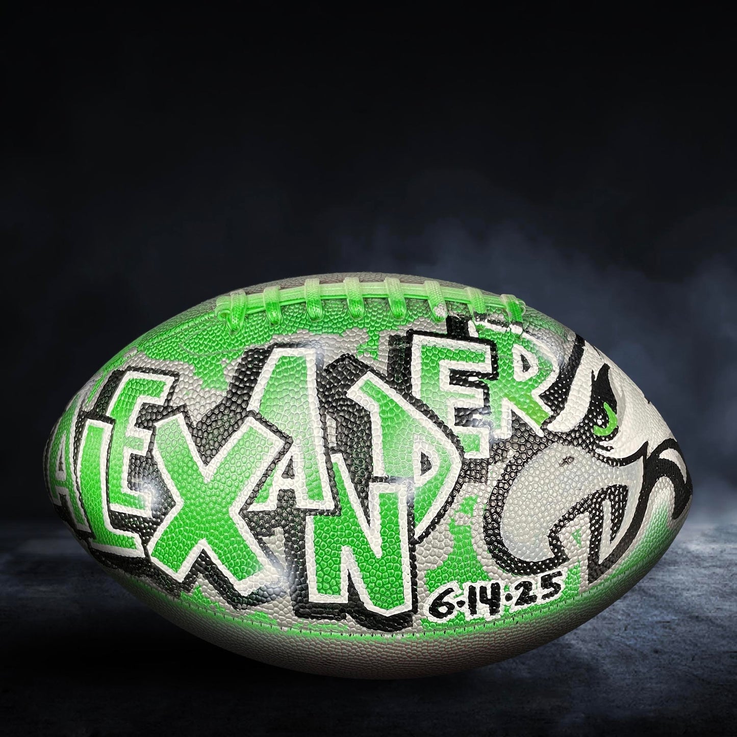 A football with the name "LEXANDER" painted on it, featuring a green and black color scheme.