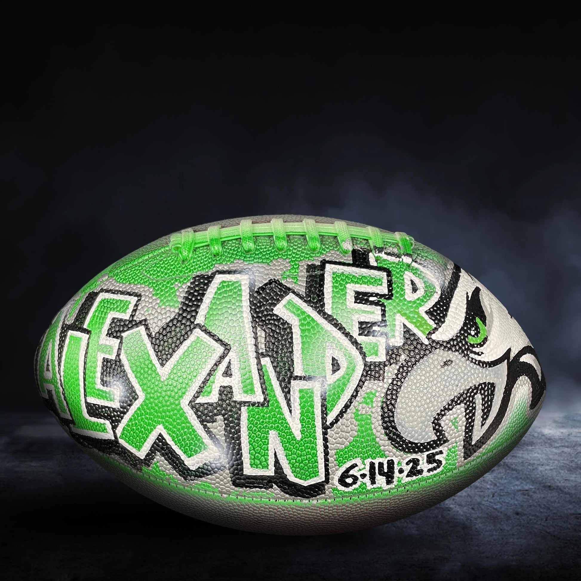 A football with the name "LEXANDER" painted on it, featuring a green and black color scheme.