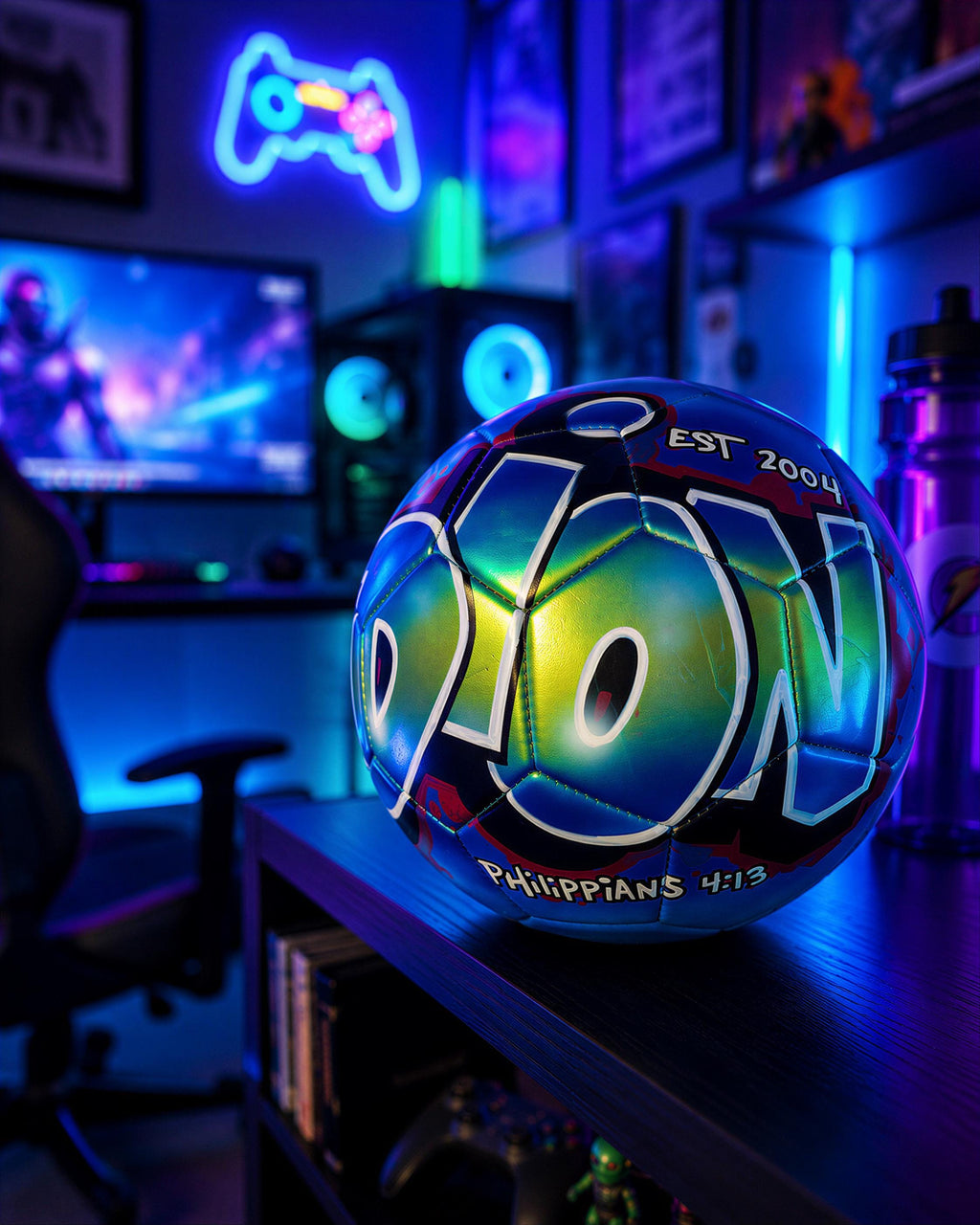 A neon-lit soccer ball with the word "DON" on it, placed on a shelf in a brightly lit room with gaming equipment and a TV in the background.