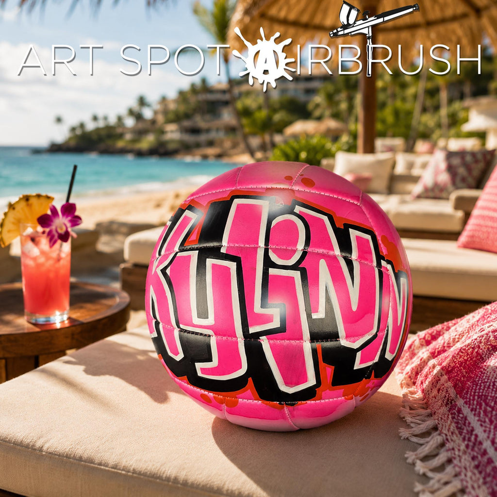 A pink and black airbrushed custom volleyball personalizedvolleyball with the word "Kylinn" written on it, placed on a beach chair with a tropical drink in the background.