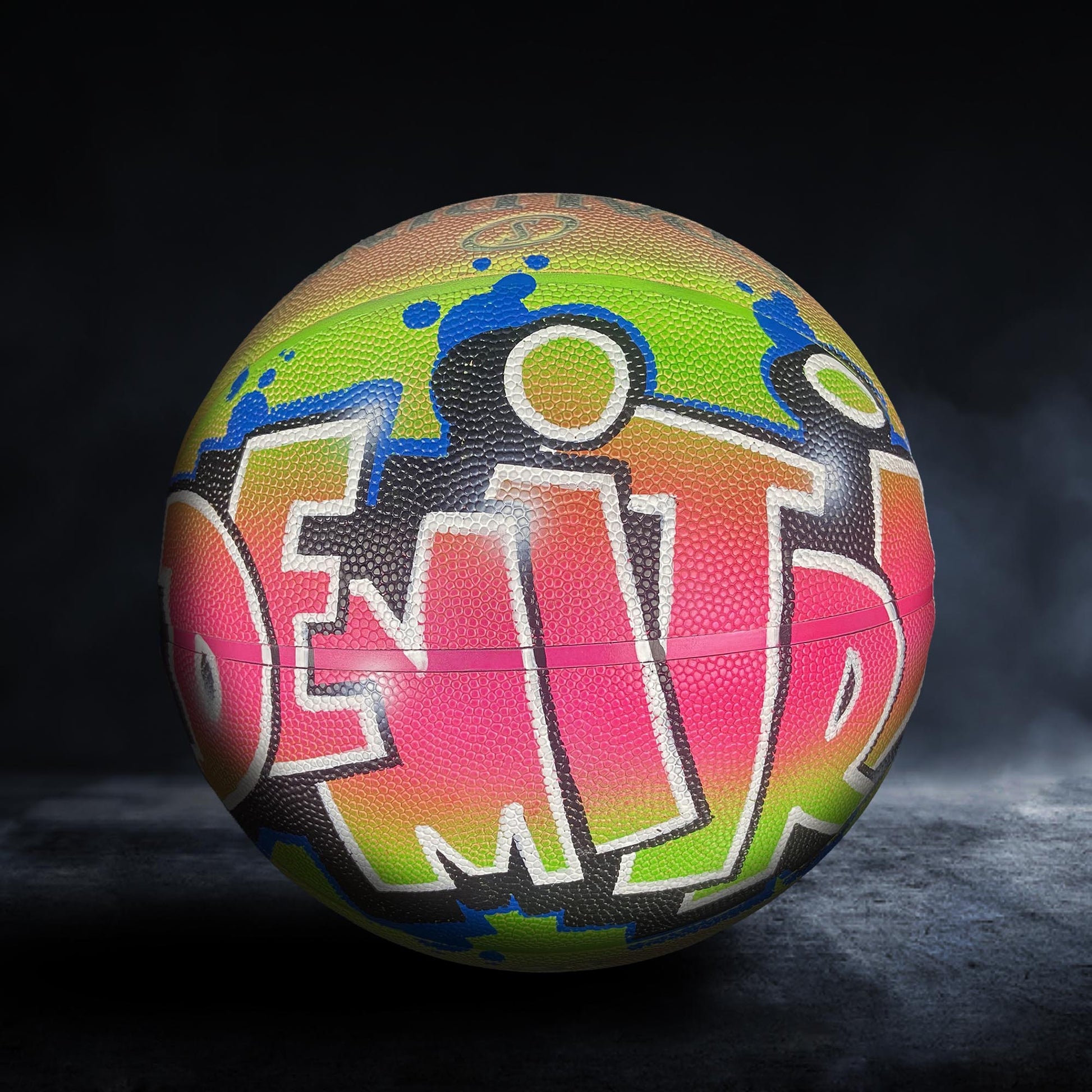 A colorful basketball with graffiti-style writing on it, sitting on a dark surface.