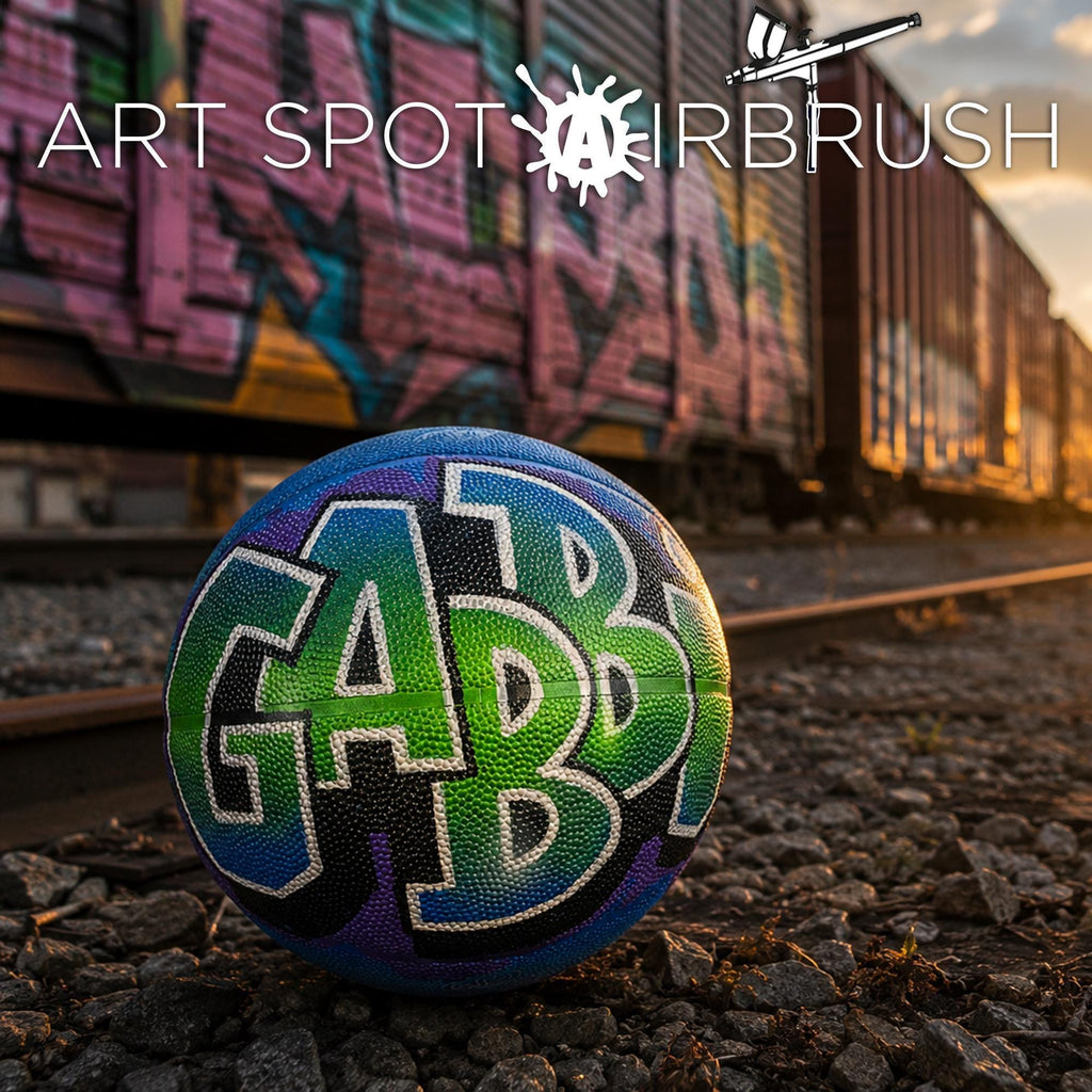 a colorful basketball with the word "GAB" painted on it, sitting on a gravel surface in front of a graffiti-covered train car.
