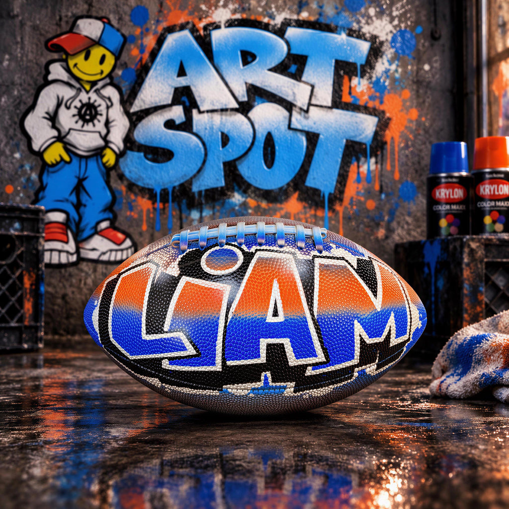 A football with the name "Liam" painted on it, sitting on a reflective surface in front of a graffiti-covered wall.