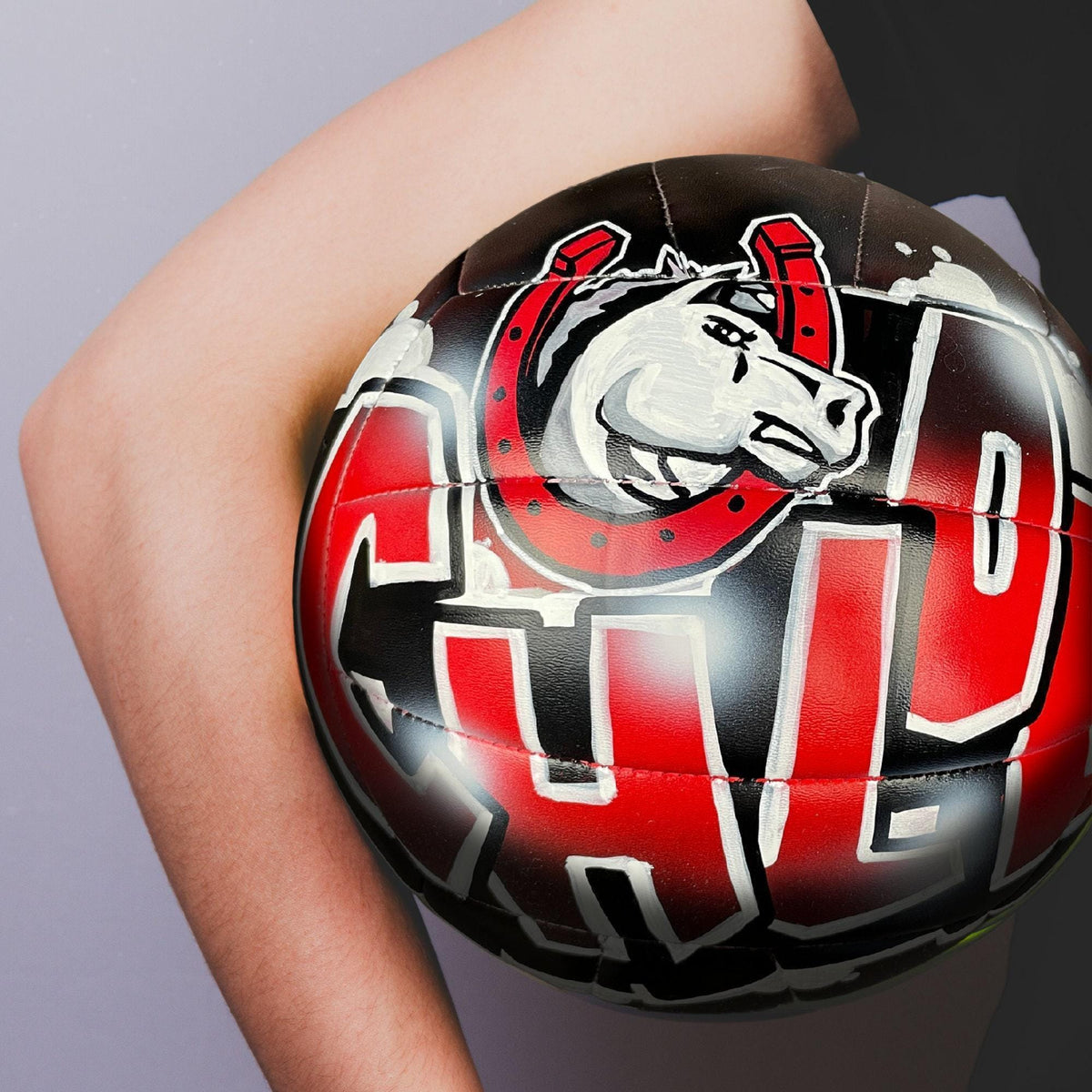 A close-up of a person's arm holding a custom volleyball personalized with a graphic design on it.