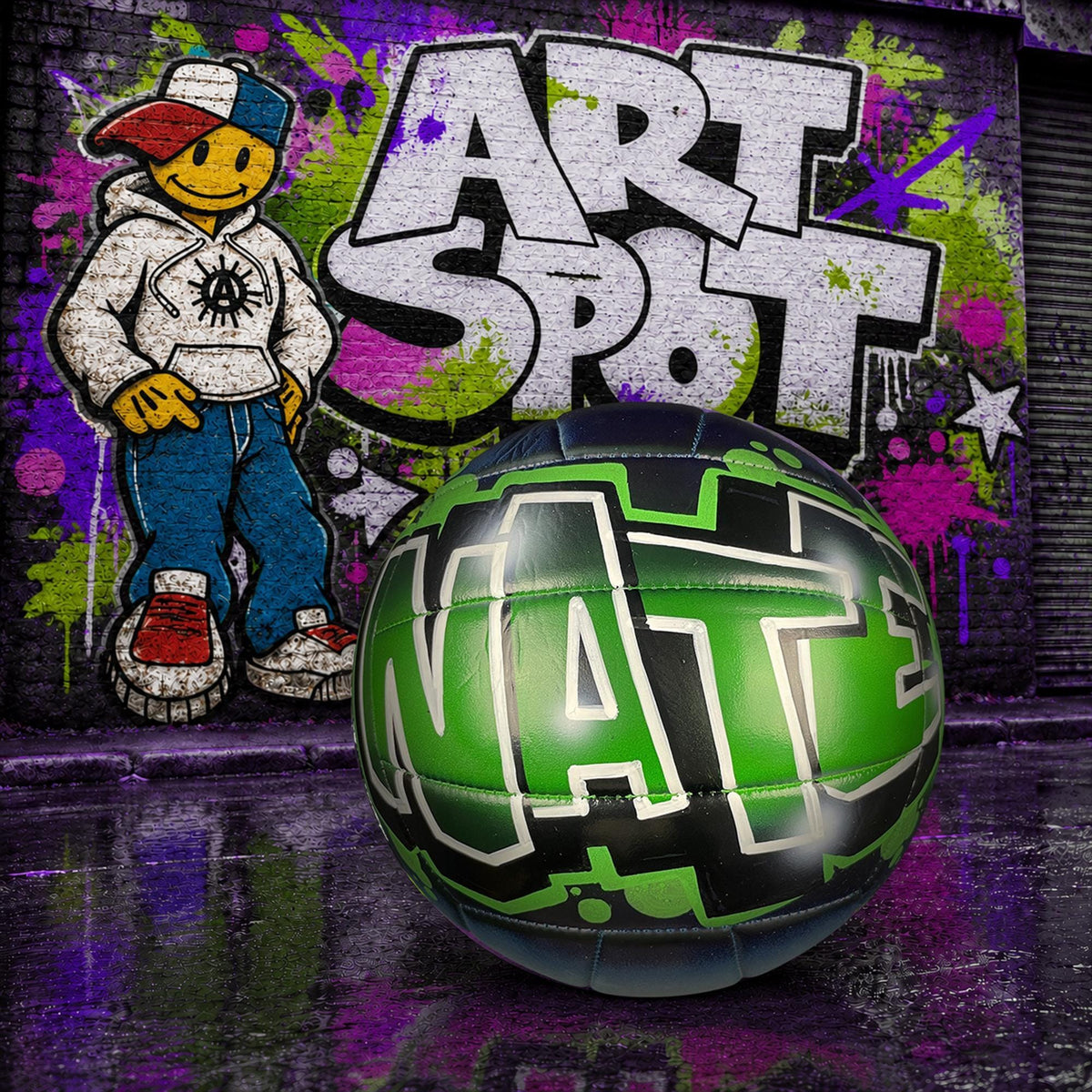 a green and black custom volleyball personalized with the word "Nate" written on it, placed in front of a graffiti mural with the name Art Spot with a cartoon character.