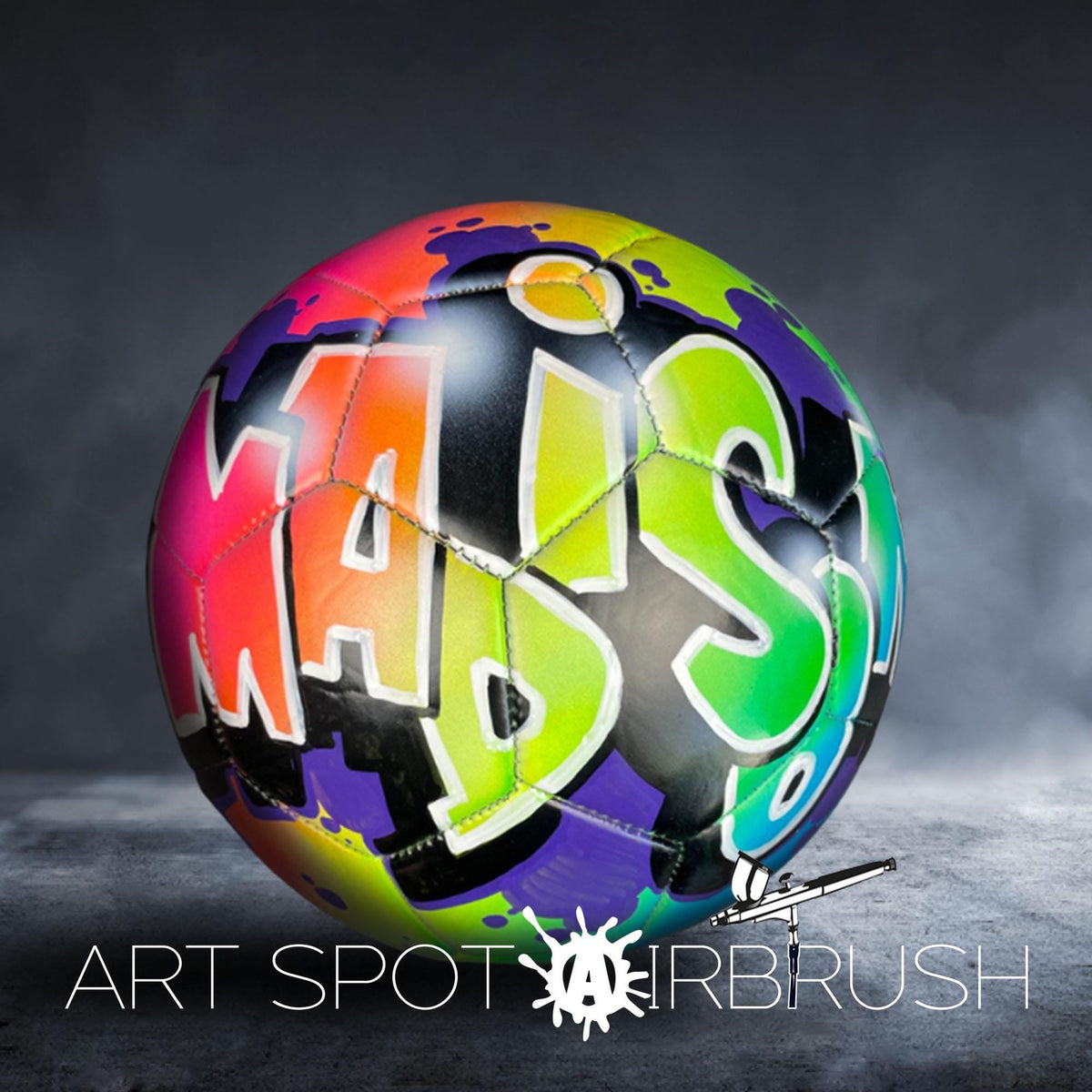 A colorful soccer ball with graffiti-style lettering on it, placed on a dark surface.